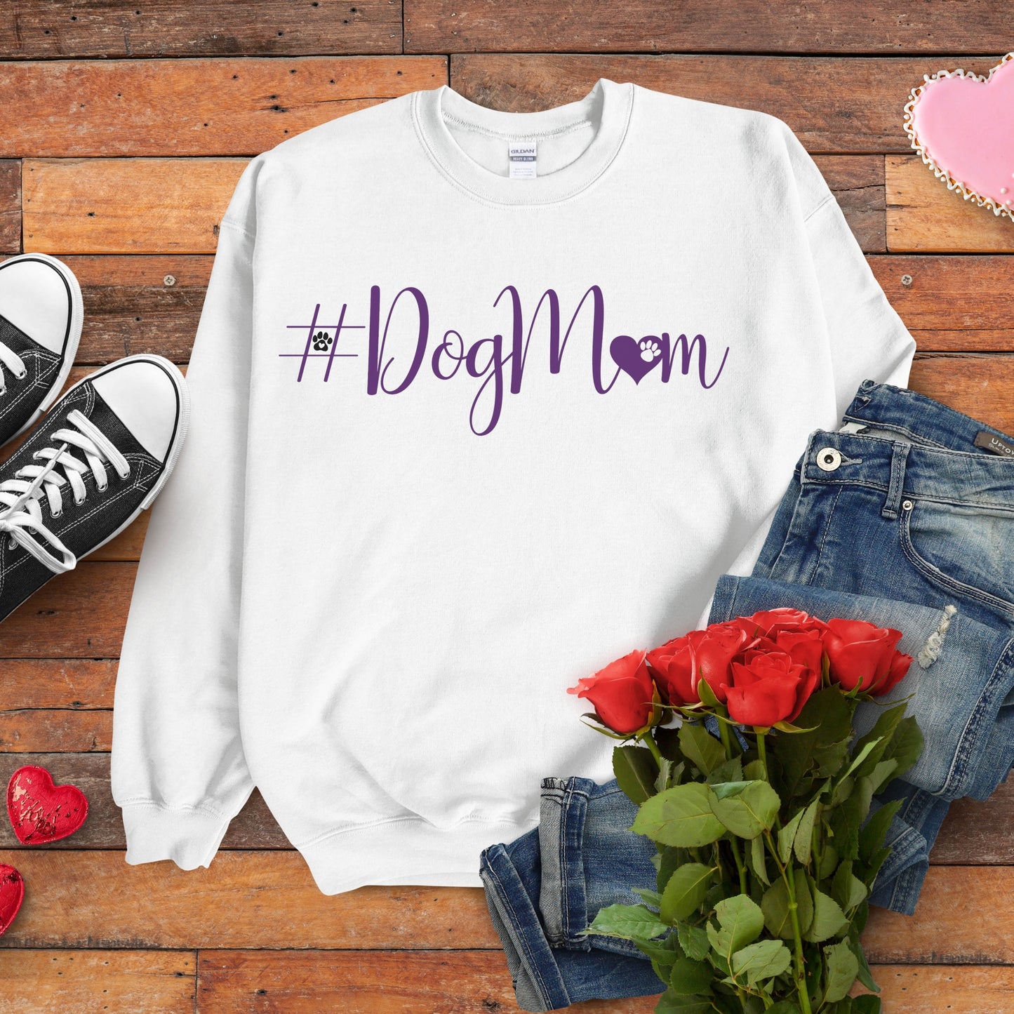 White sweatshirt with '#DogMom' text on a wooden surface with jeans, shoes, and roses.