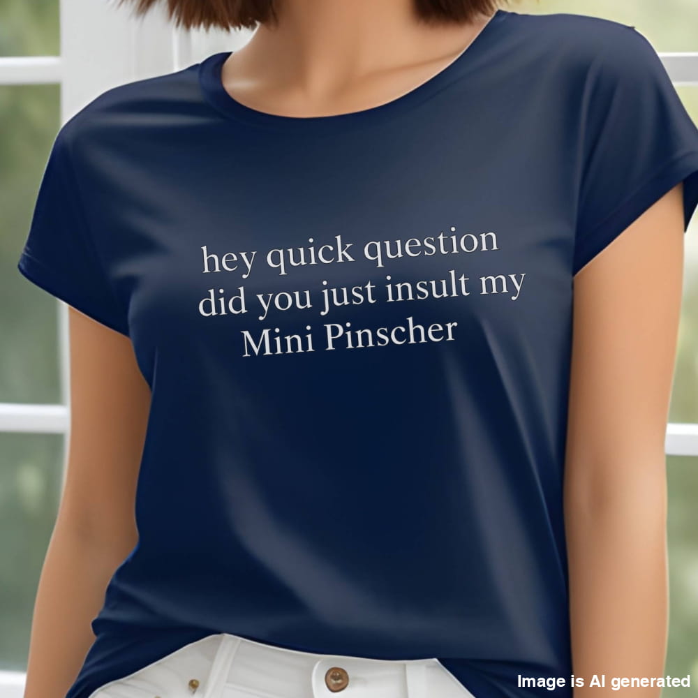 Woman wearing a navy "hey quick question did you just insult my Mini Pinscher" t-shirt, standing by a window