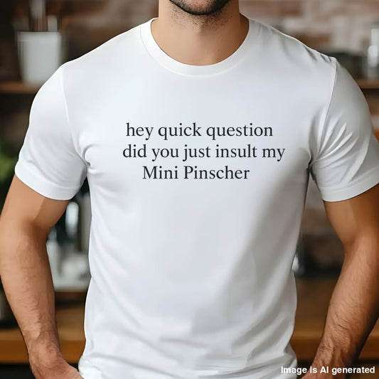 Man wearing a white "hey quick question did you just insult my Mini Pinscher" t-shirt, standing by a window