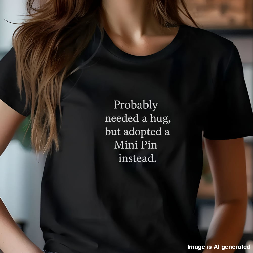Black unisex t-shirt with white text: "Probably needed a hug, but adopted a Mini Pin instead." displayed on plain background 