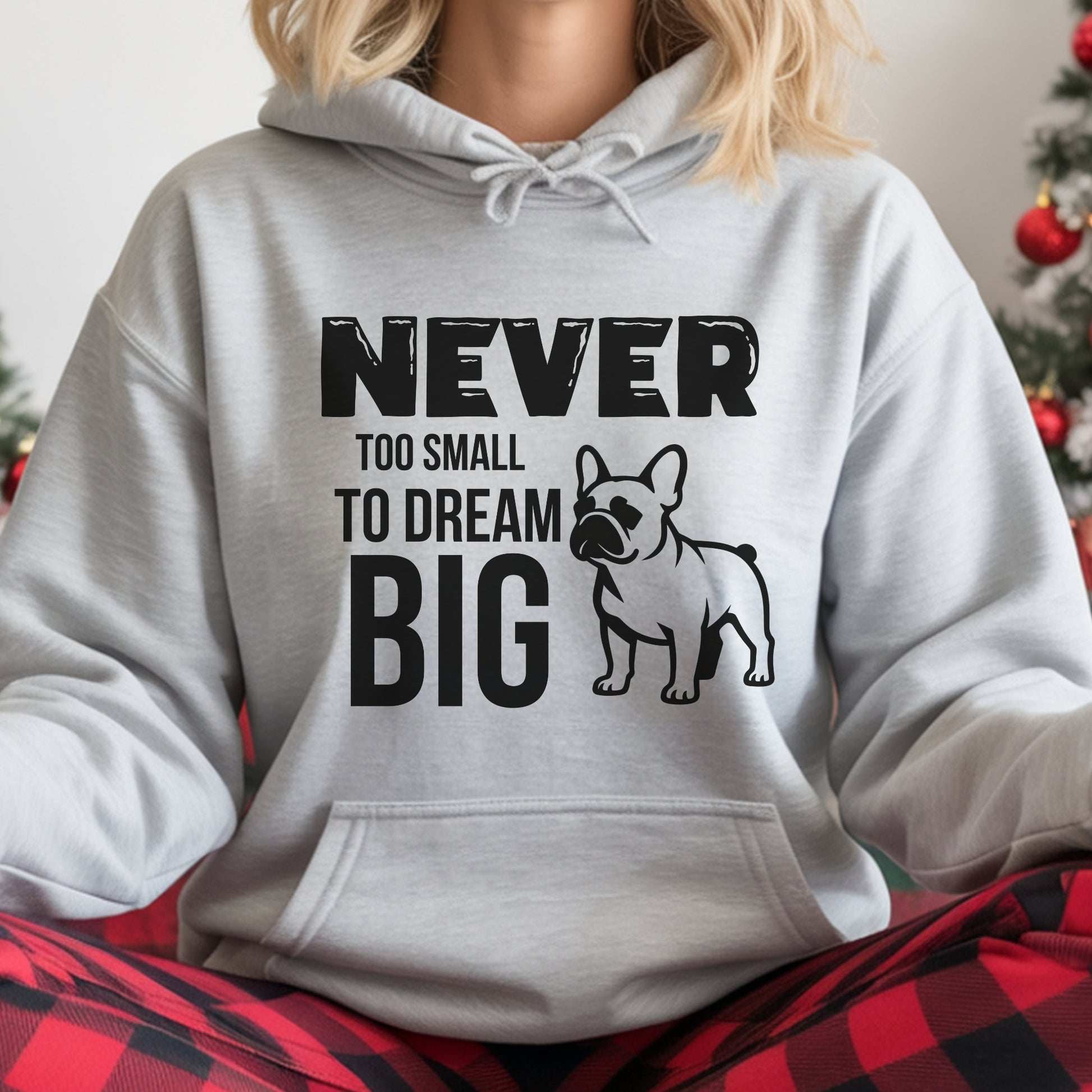 Person wearing a gray hoodie with a motivational quote and dog illustration, sitting in front of a Christmas tree.