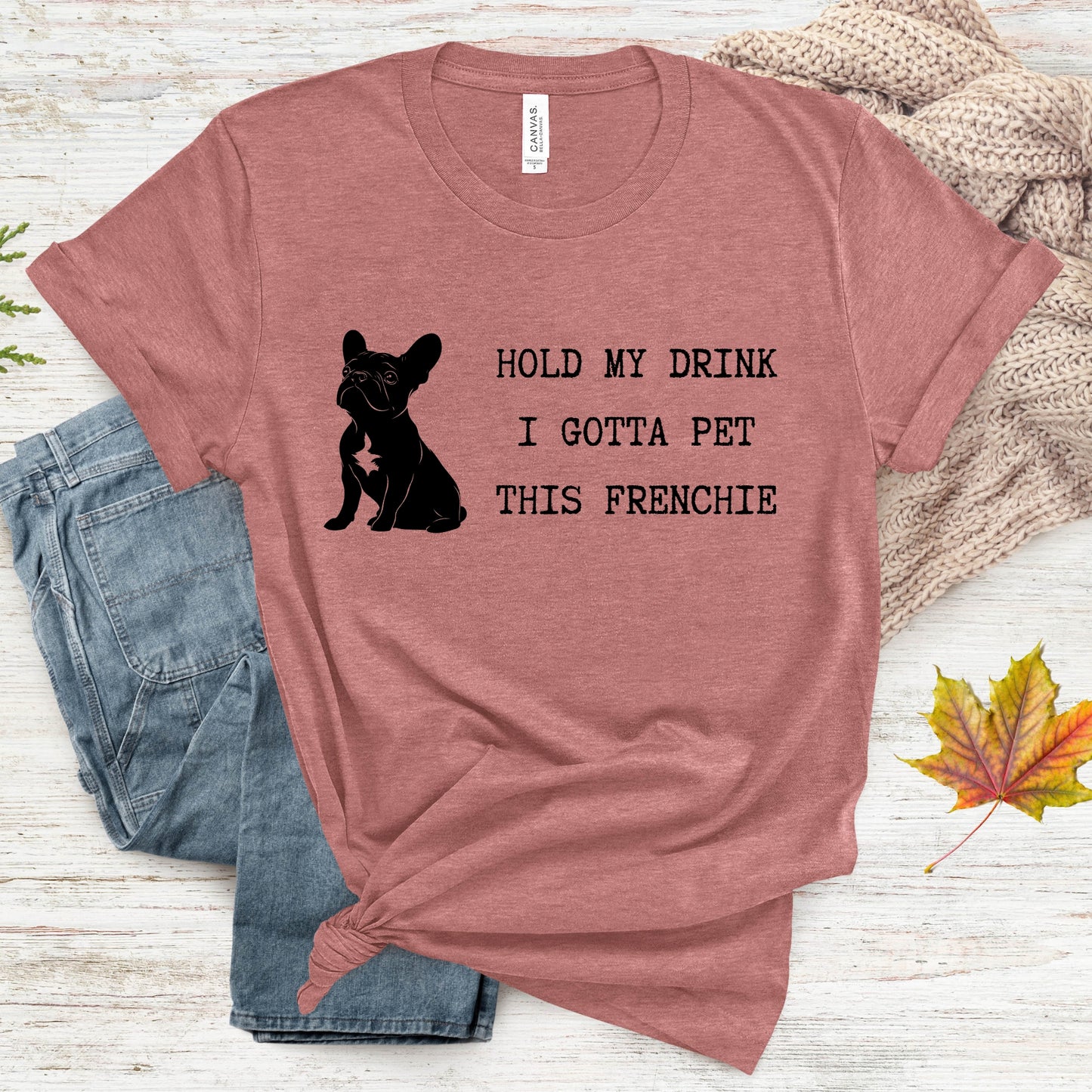 Mauve t-shirt with a black dog graphic and text on a wooden surface with jeans and leaves.