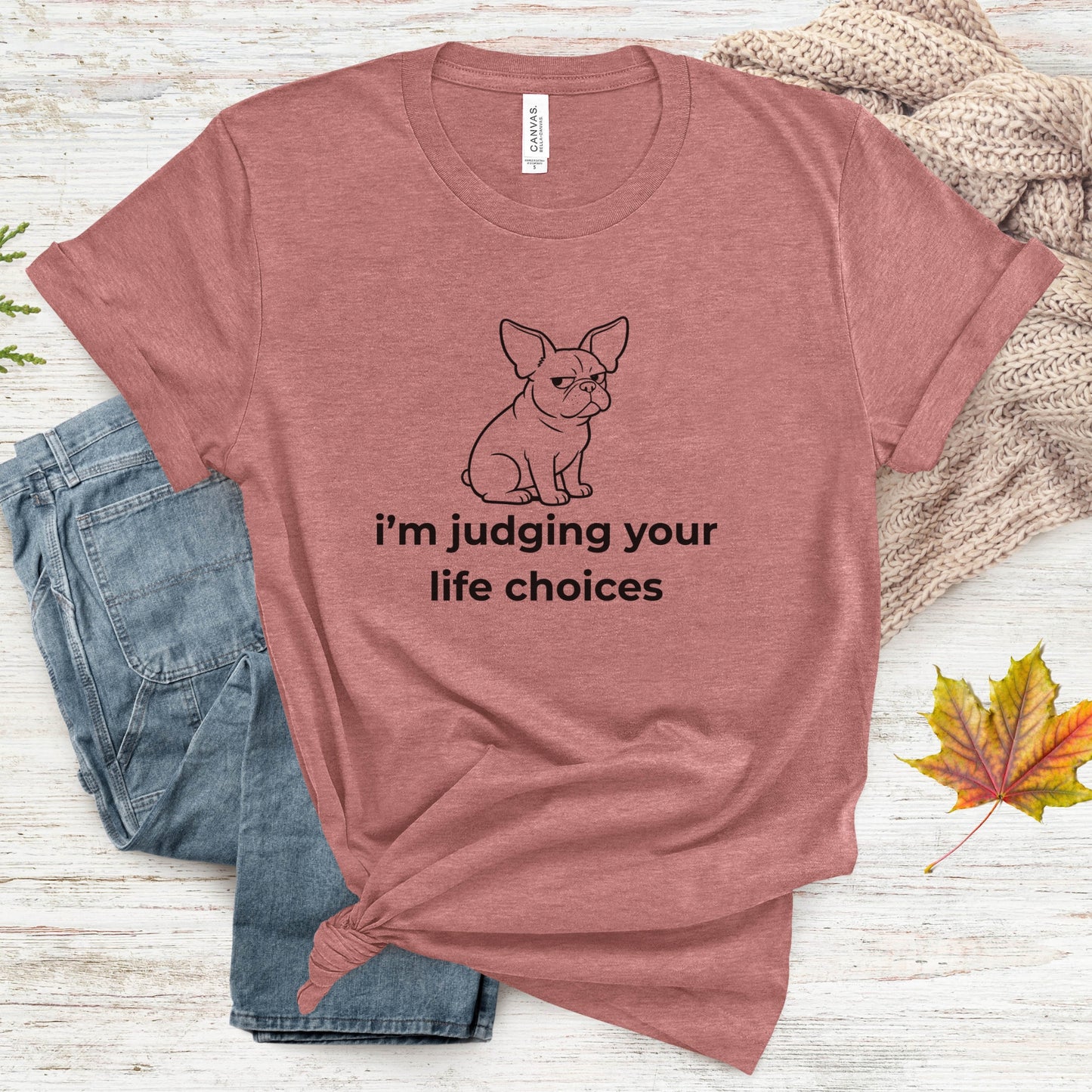 Mauve t-shirt with a dog graphic and text on a wooden surface with jeans and leaves.