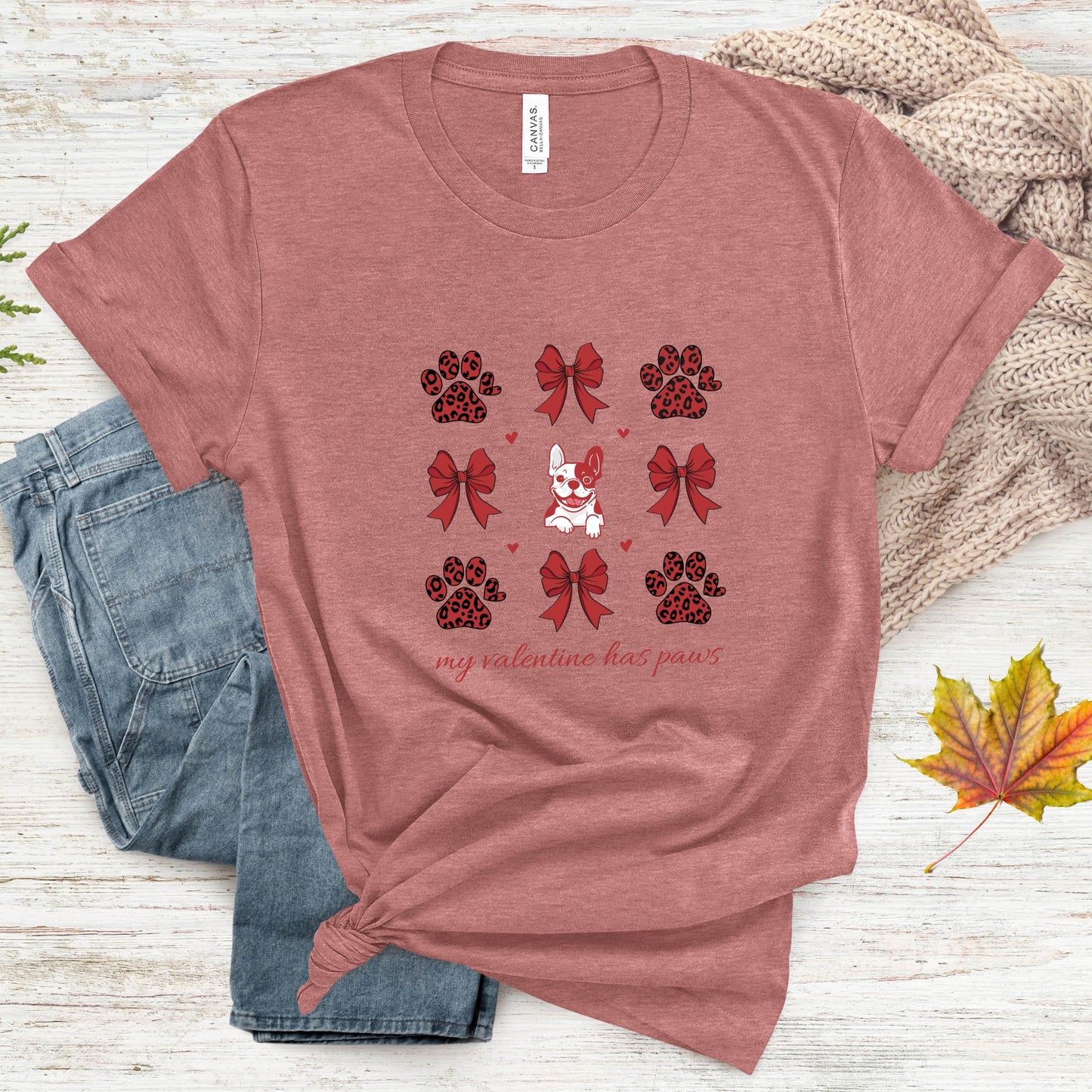 Heather mauve t-shirt with paw and bow design on a wooden surface with jeans and leaves.