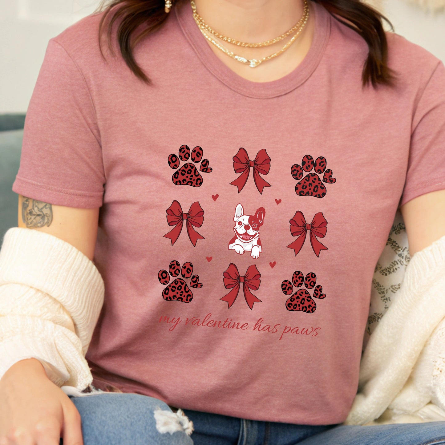 Person wearing a heather mauve t-shirt with paw and bow designs and text.