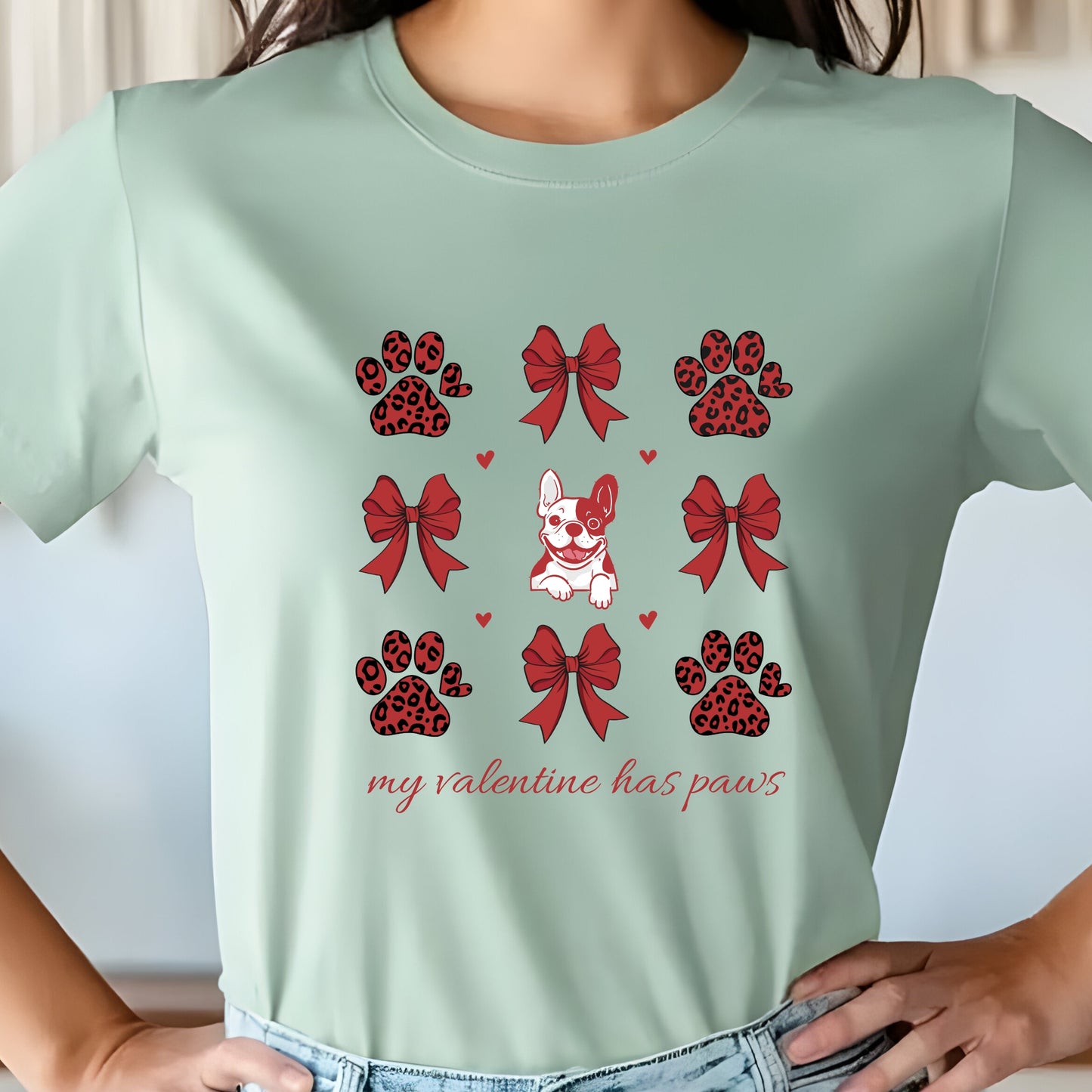 Light green t-shirt with red and black paw prints, bows, and a dog illustration on a white background.