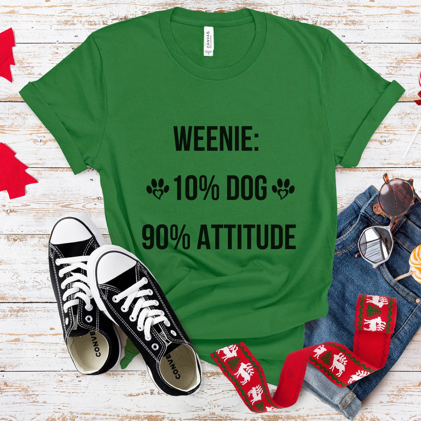 Green t-shirt with 'WEENIE: 10% DOG 90% ATTITUDE' text, black sneakers, red and white socks, and a small dog on a wooden surface.