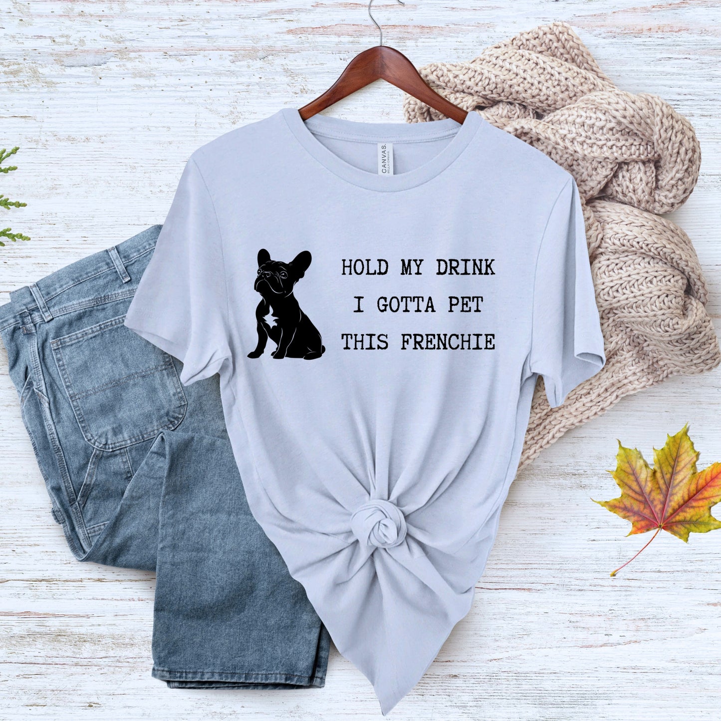 Gray t-shirt with a dog graphic and text on a wooden surface with jeans and a sweater.