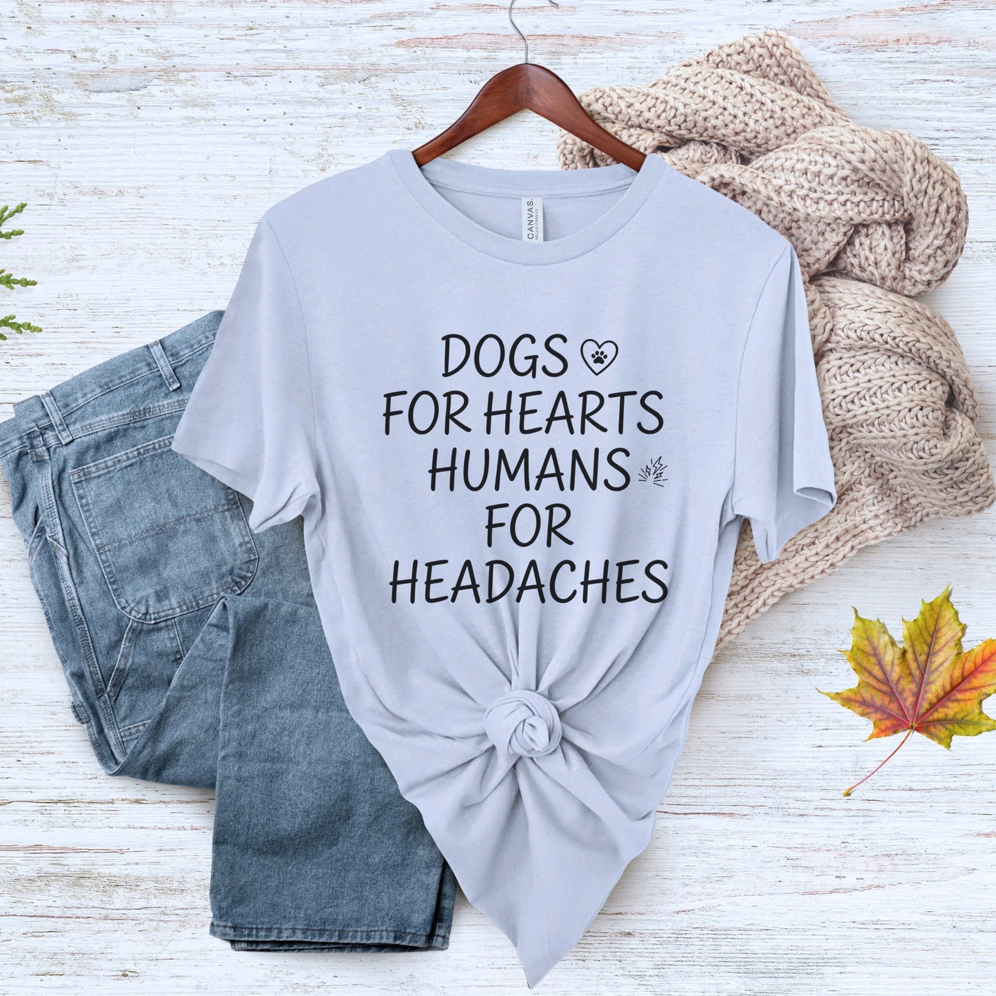 Gray t-shirt with 'Dogs for hearts, humans for headaches' text on a wooden surface with jeans and a sweater.