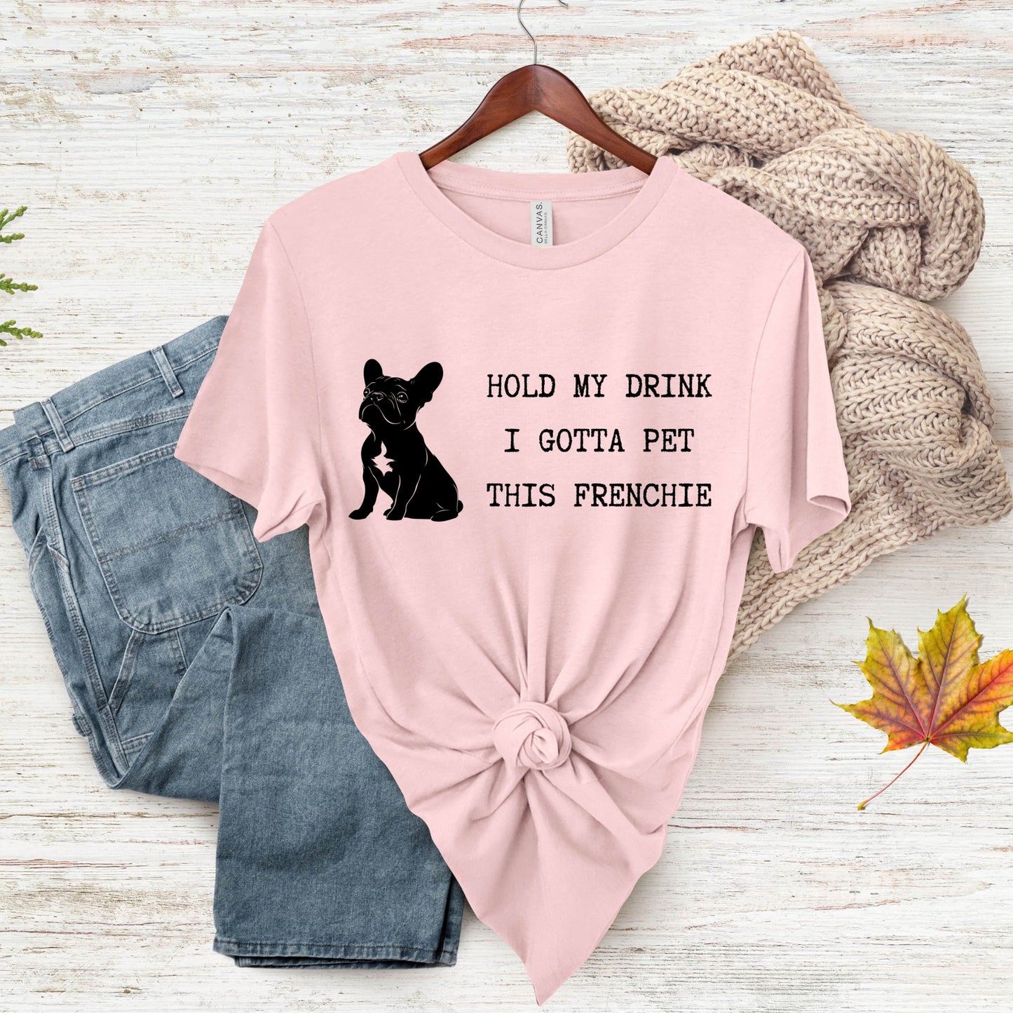 Pink t-shirt with a dog graphic and text on a wooden surface with jeans and a sweater.