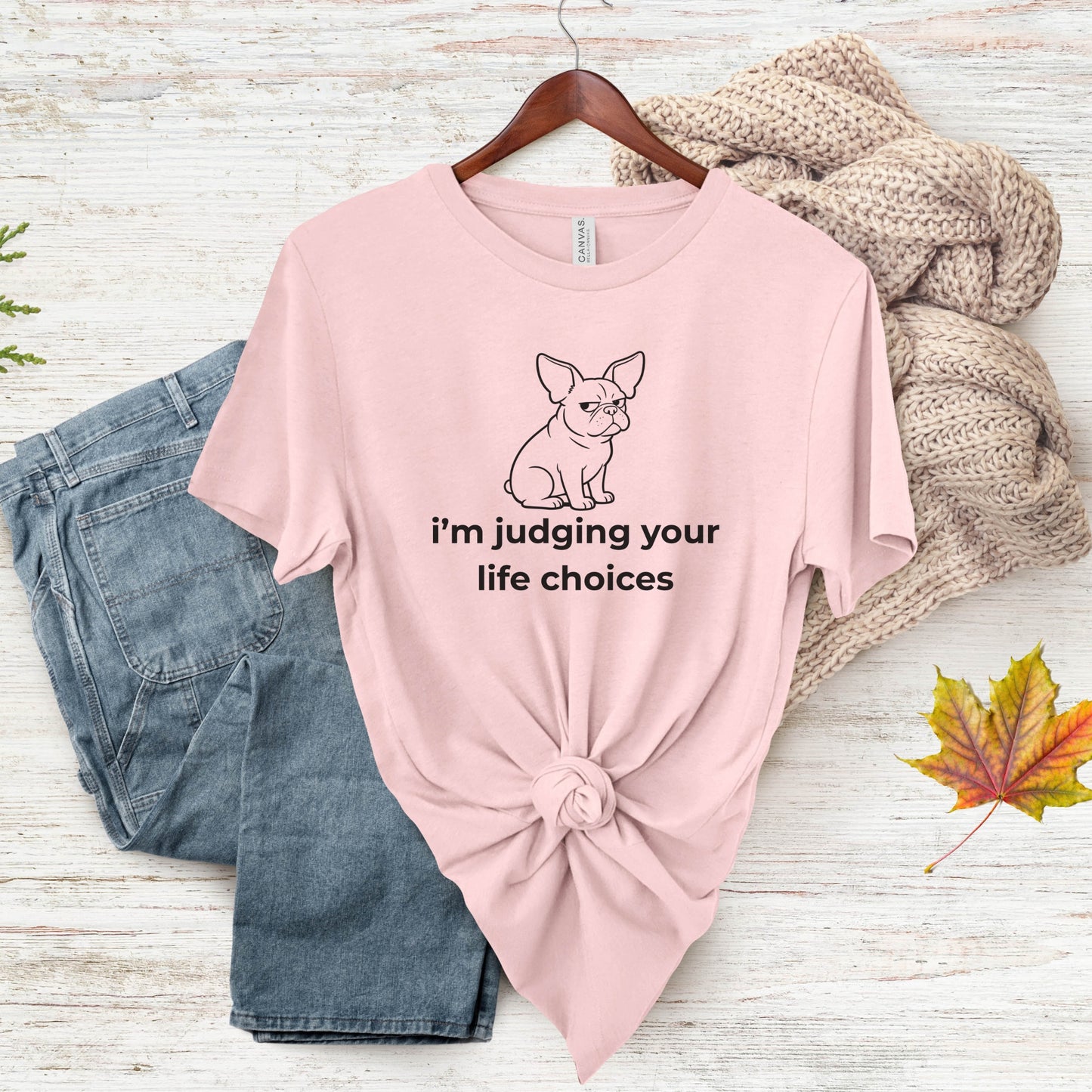 Pink t-shirt with a graphic and text, paired with jeans and a sweater on a wooden surface.