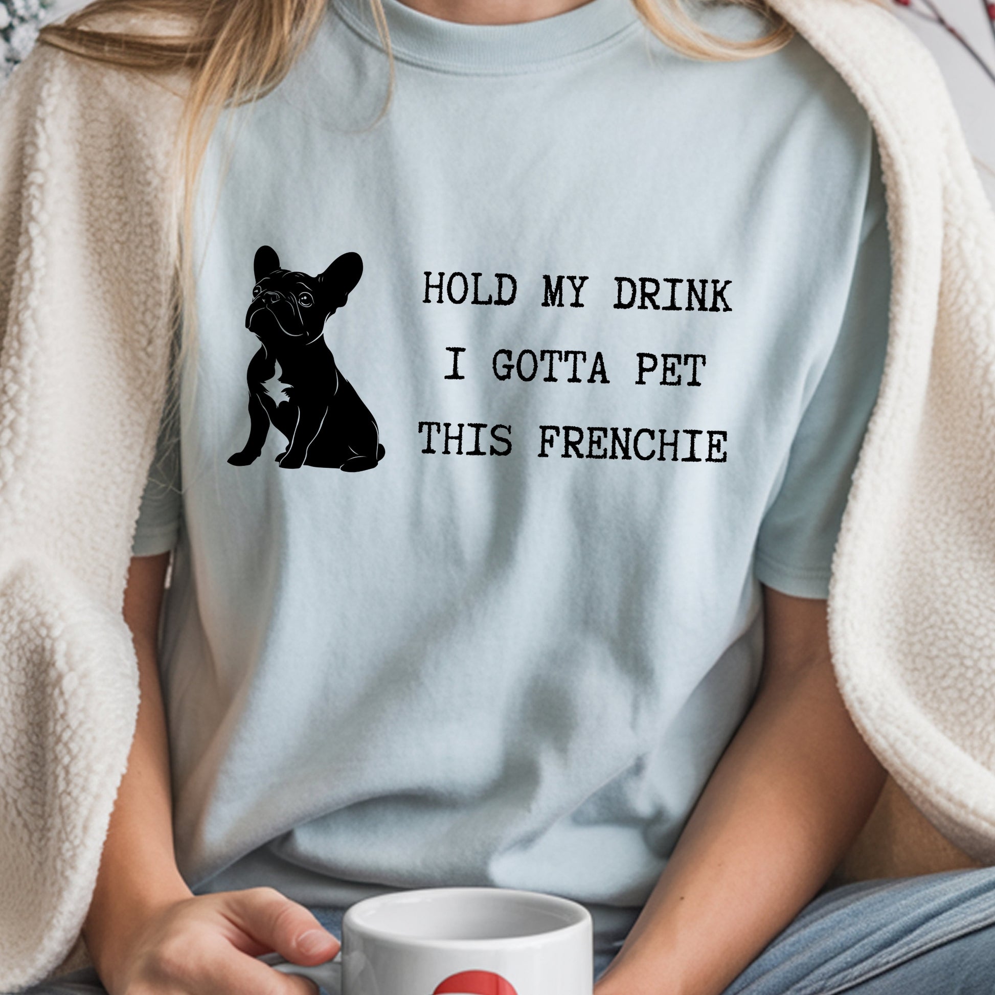 Person wearing a light blue t-shirt with a dog graphic and text, holding a mug.