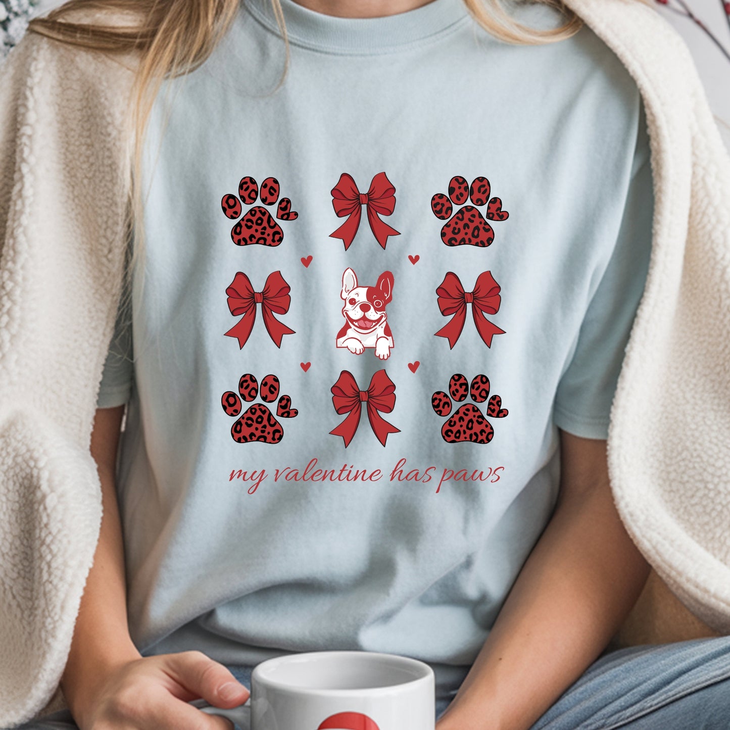 Person wearing a light blue t-shirt with Valentine's Day-themed designs, holding a mug.