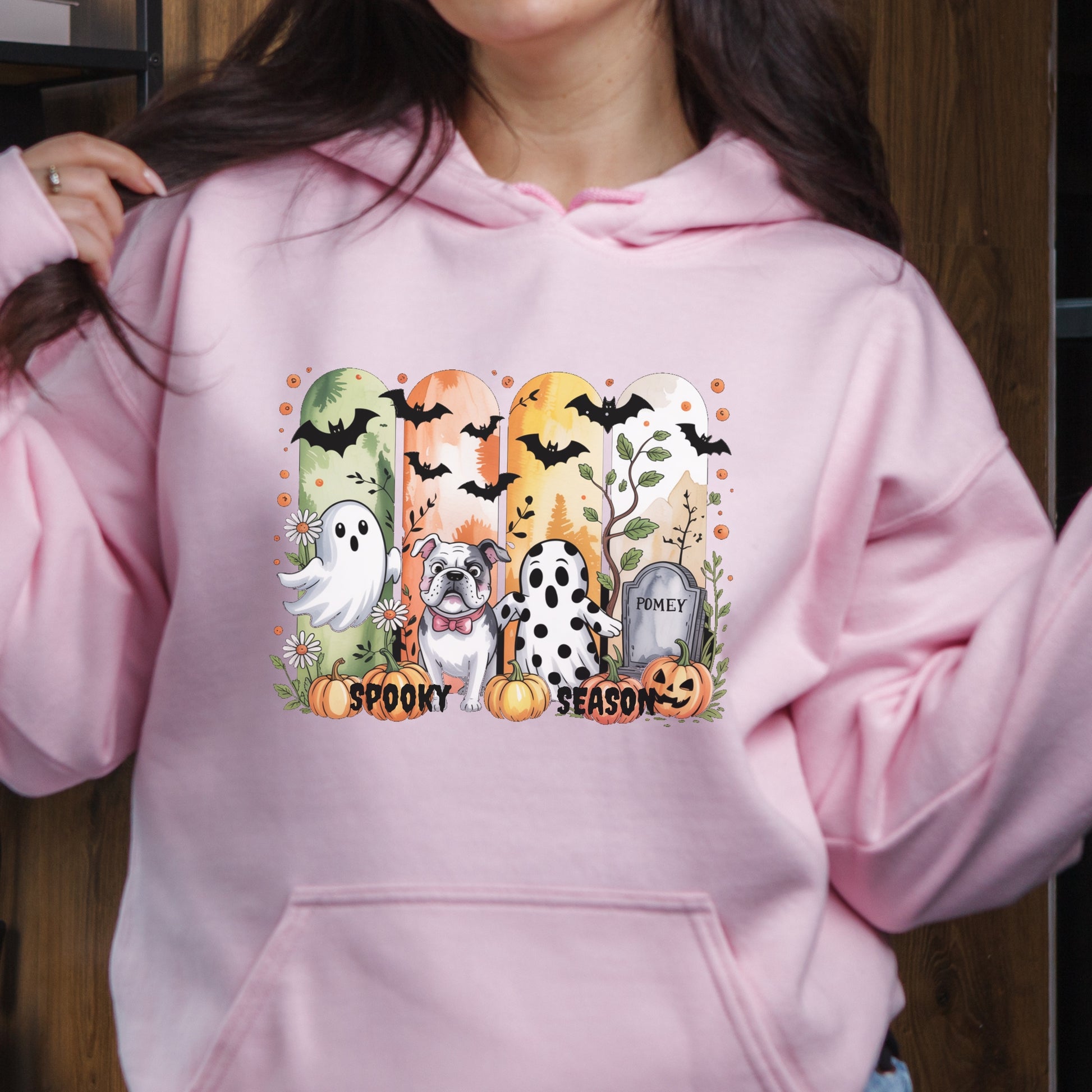 Light pink hoodie with Halloween-themed print of small dogs in ghost costumes, bats, pumpkins, and “Spooky Season” text on the front.