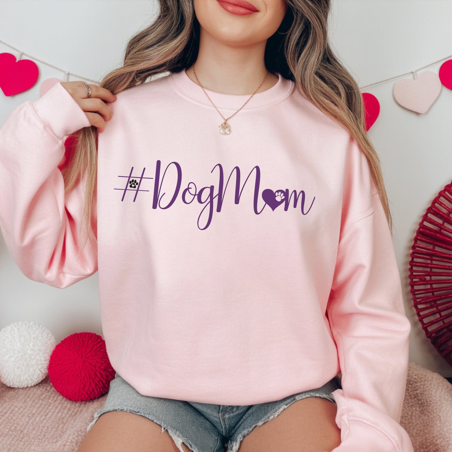 Person wearing a pink sweatshirt with '#DogMom' text, sitting against a decorative background.