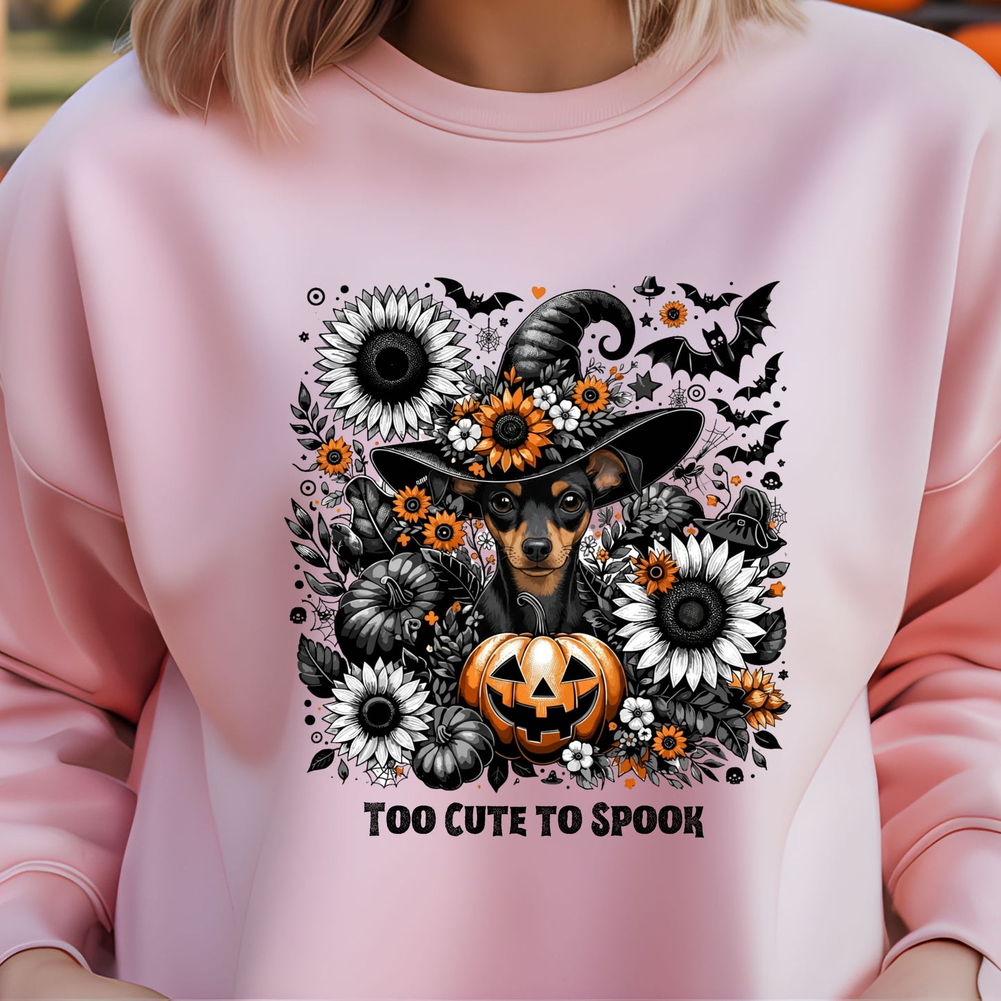 Pink sweatshirt with Halloween-themed design featuring a dog in a witch hat, pumpkins, and flowers.