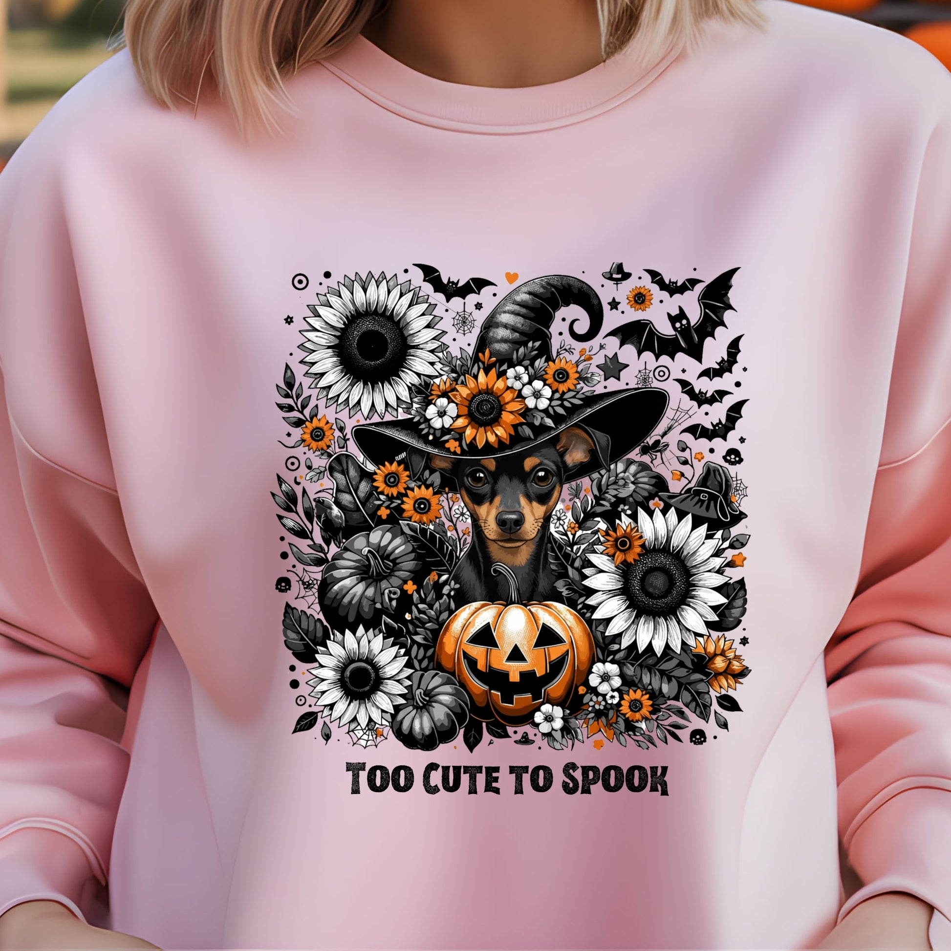 Pink sweatshirt with Halloween-themed design featuring a dog in a witch hat, pumpkins, and flowers.