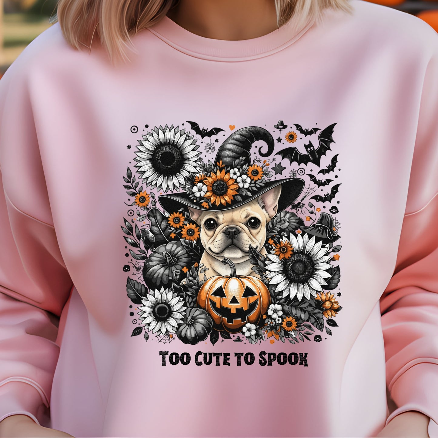 Pink sweatshirt with a Halloween-themed design featuring a dog in a witch hat and pumpkin, surrounded by flowers and text 'Too Cute To Spook'.