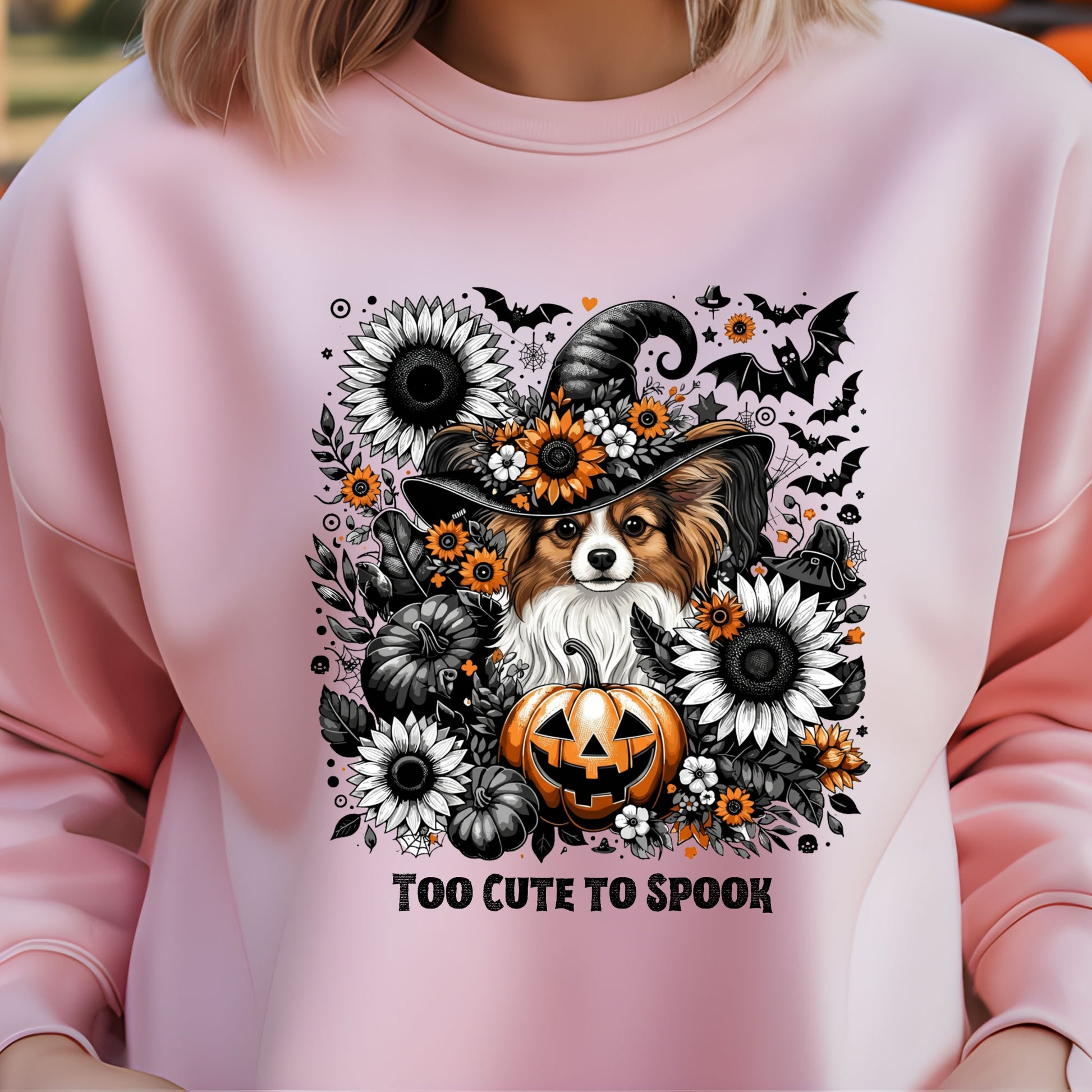 Pink sweatshirt with a Halloween-themed design featuring a dog in a witch hat, pumpkins, and flowers.