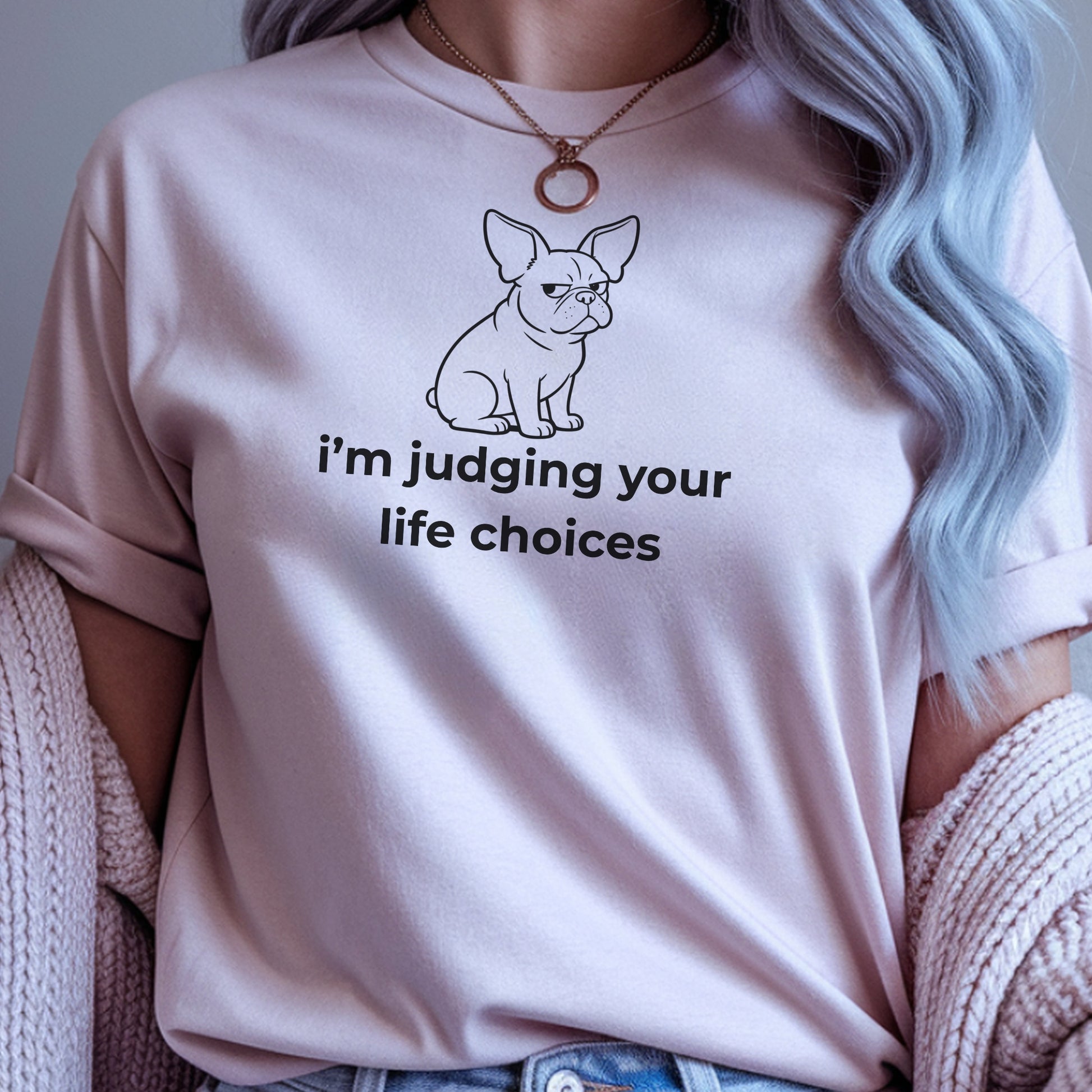 Person wearing a light pink t-shirt with a dog graphic and text, sitting on a textured surface.