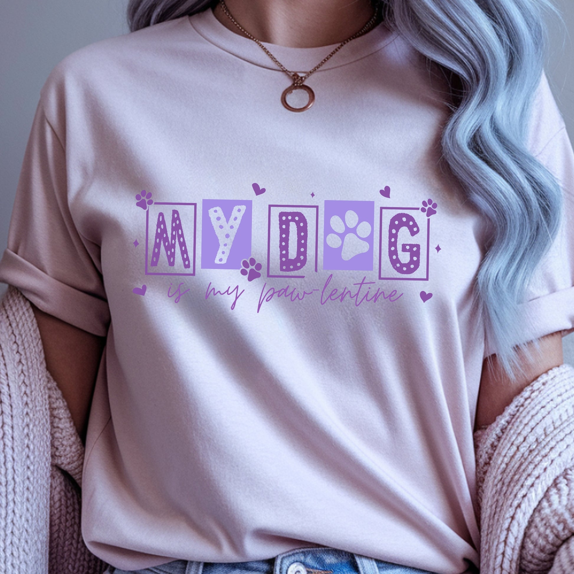 Person wearing a light pink t-shirt with purple text 'MY DOG is my paw-lentine' and paw print design.