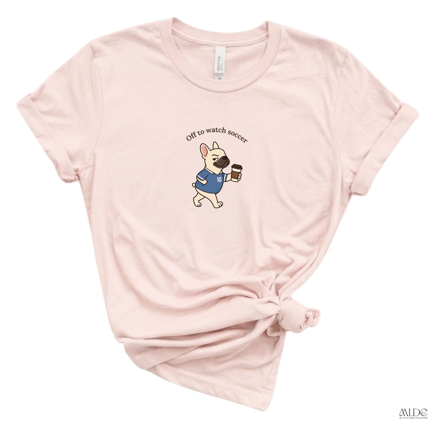 Pink t-shirt with a dog graphic and text 'Off to watch soccer' on a white background
