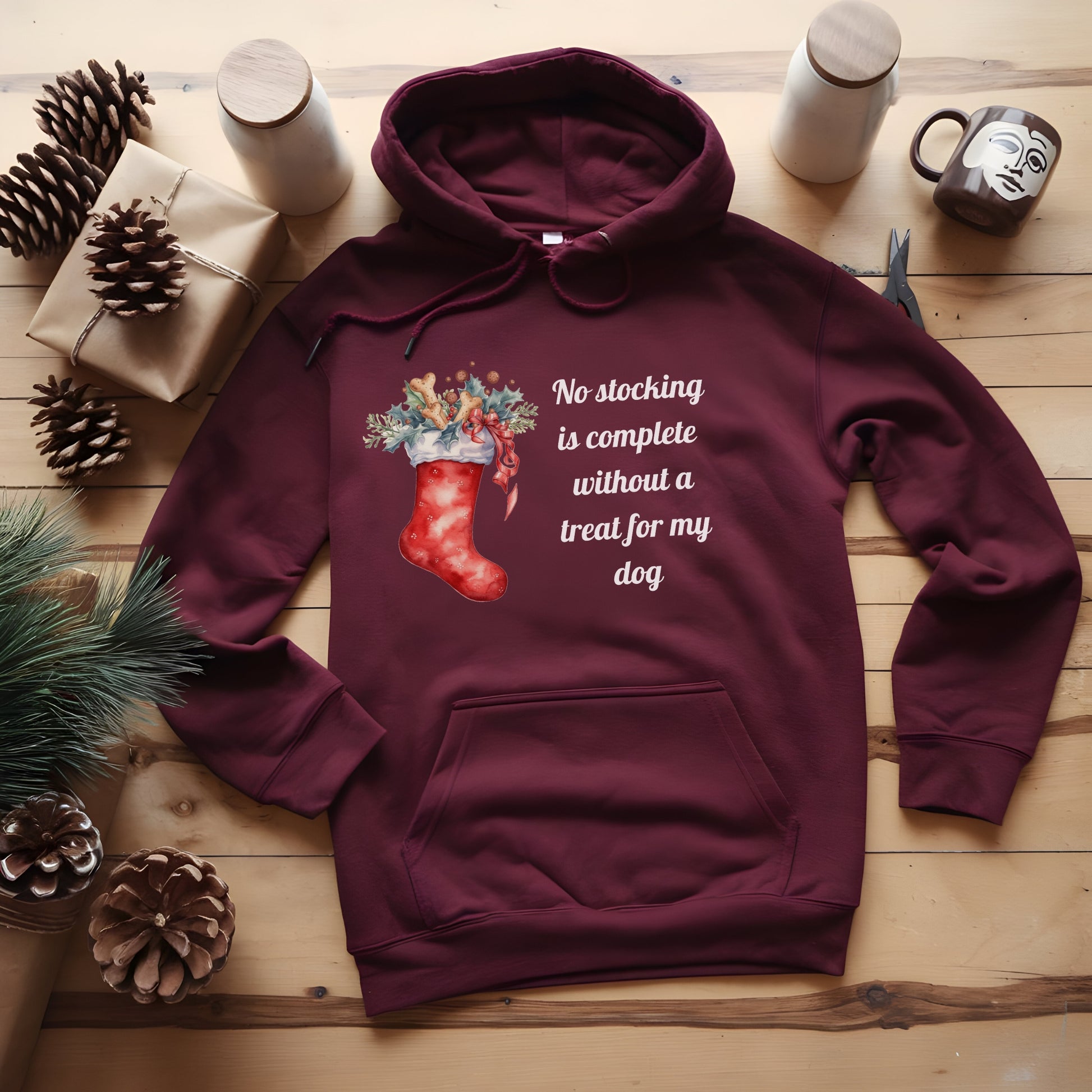 Maroon hoodie with Christmas design and text on a wooden surface with decorative items.