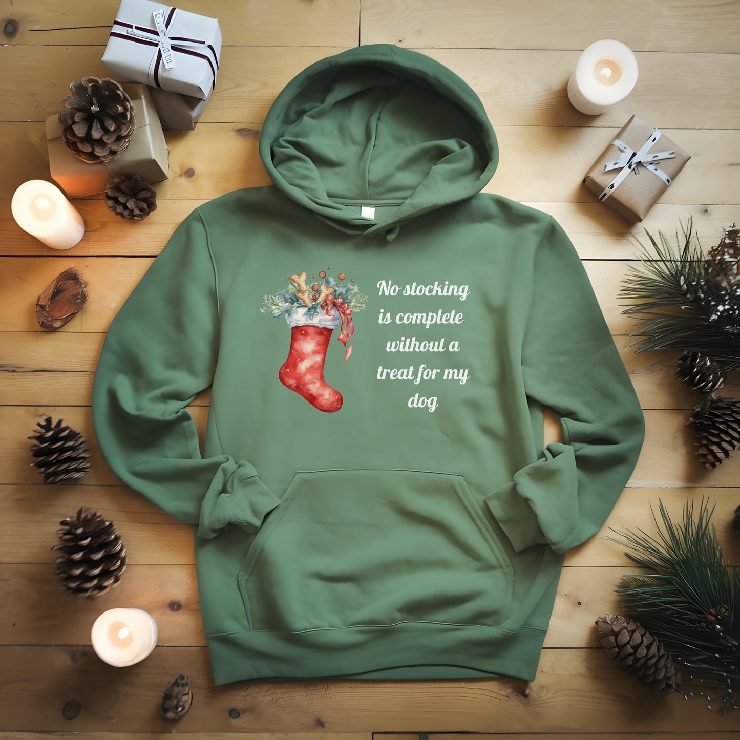 Green hoodie with Christmas design and text on a wooden surface with candles and pinecones.