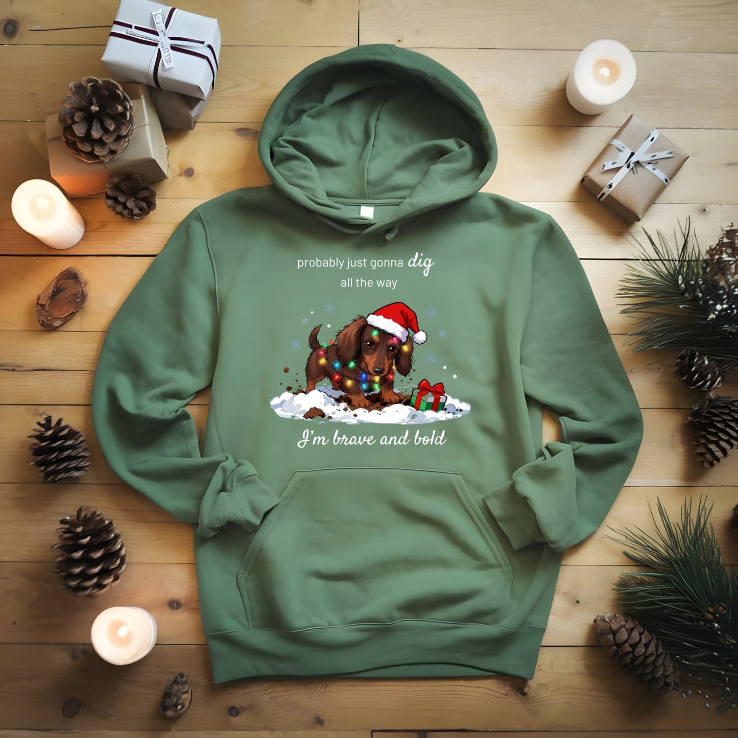 Green hoodie with a Christmas-themed design on a wooden surface with candles and pinecones.