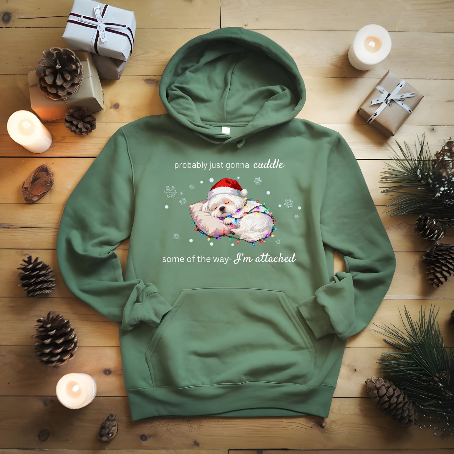 Green hoodie with a Christmas design on a wooden surface with candles and pinecones.