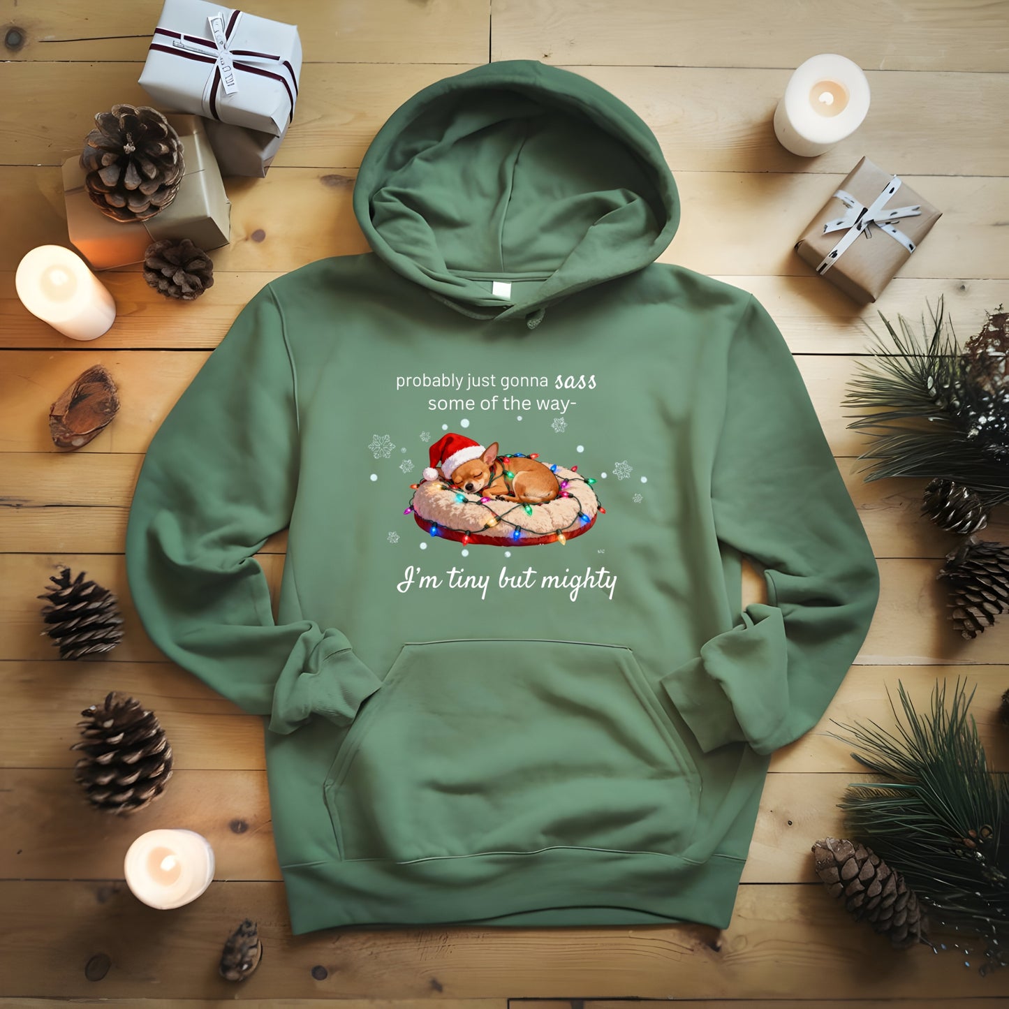 Green hoodie with a printed design on a wooden surface with candles and pinecones.