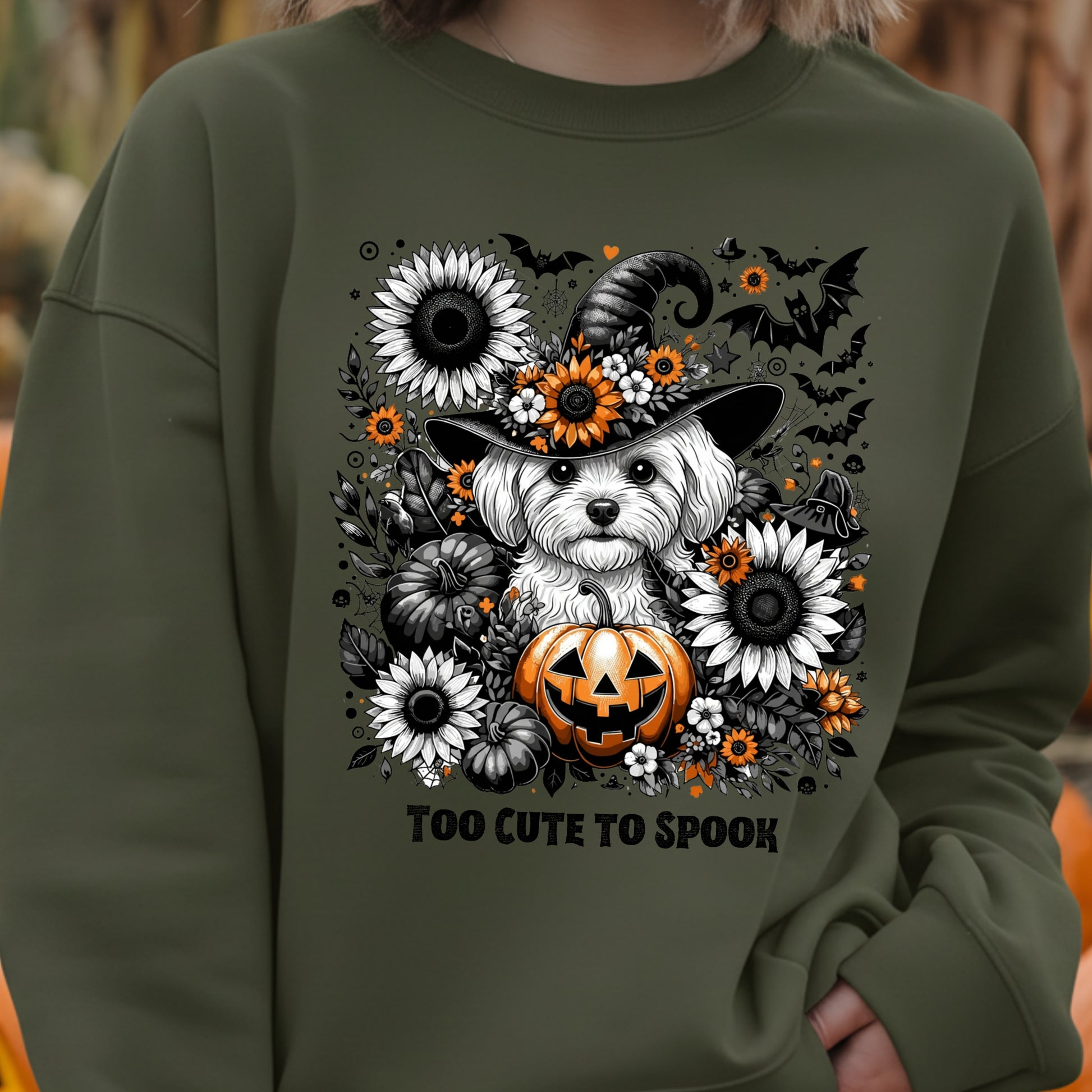 Green sweatshirt with a Halloween-themed design featuring a dog in a witch hat and pumpkin, surrounded by flowers and text 'Too Cute To Spook'.