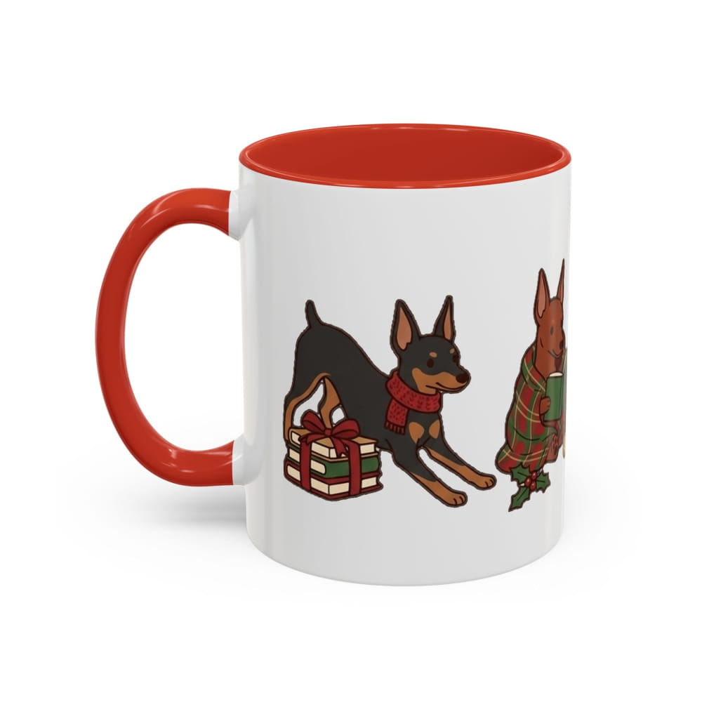 White ceramic mug with a red interior and red handle, showing a black-and-tan Mini Pinscher leaning over a wrapped gift and a red Min Pin in a plaid blanket.