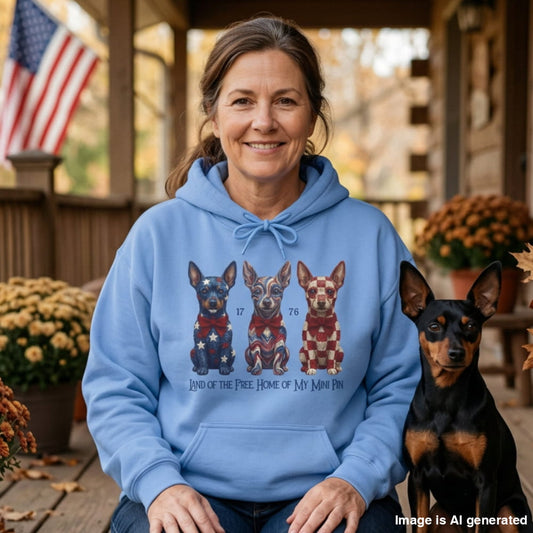 Woman in a Carolina Blue Land of the Free hoodie with three patriotic Mini Pinschers, sitting on a porch next to her Mini Pinscher