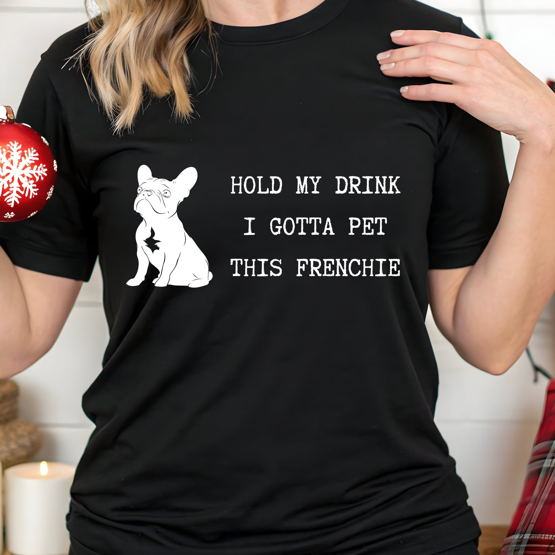 Person wearing a black t-shirt with a dog graphic and text, holding a red and white Christmas ornament.