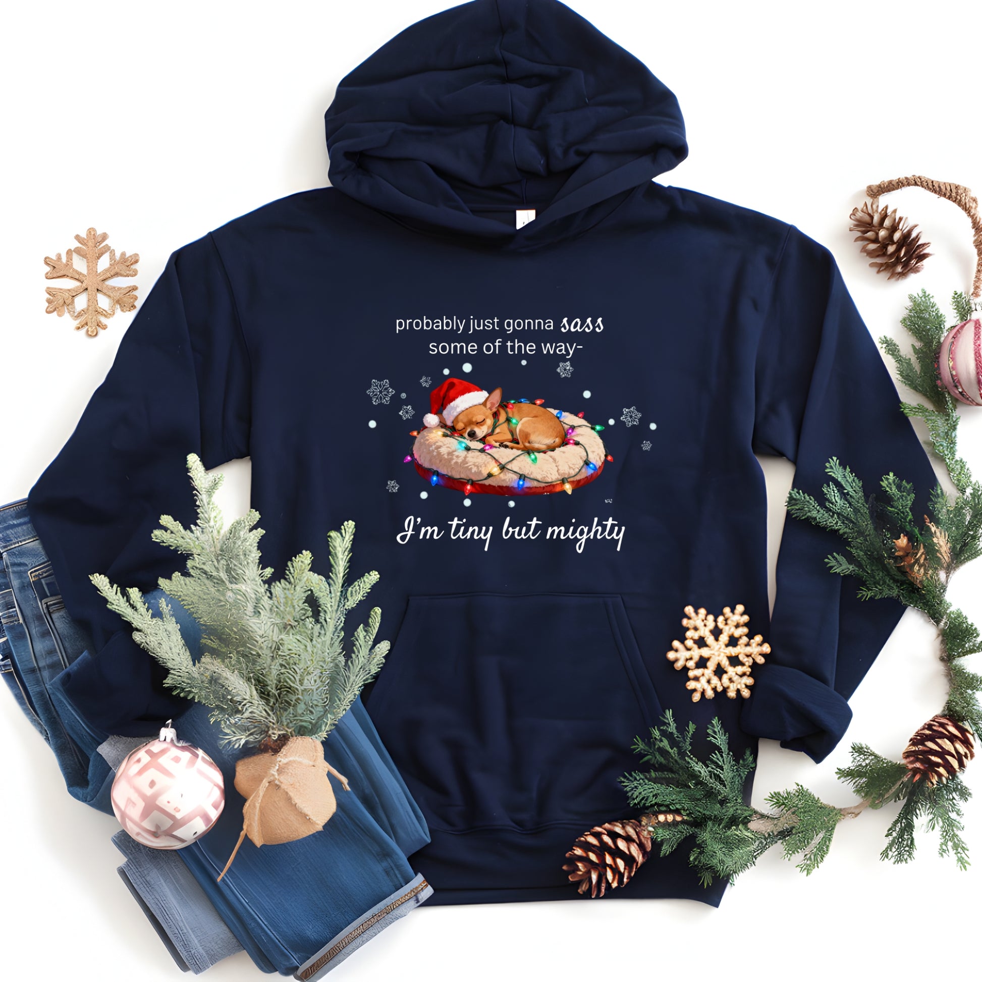 Navy blue hoodie with Christmas-themed design and text, surrounded by holiday decorations on a white background.