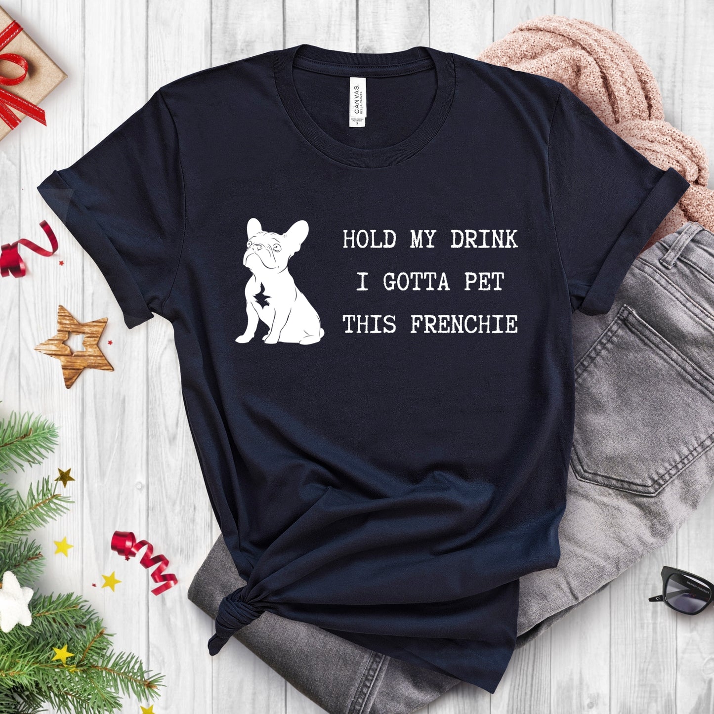 Black t-shirt with a dog graphic and text on a wooden surface with jeans and Christmas decorations.