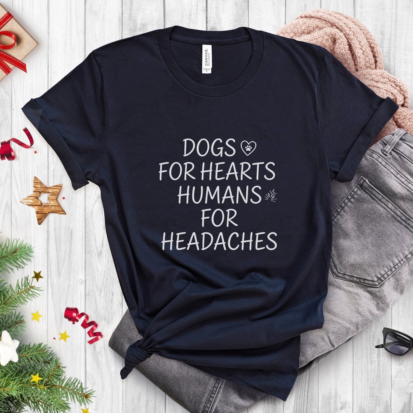 Black t-shirt with text 'DOGS FOR HEARTS HUMANS FOR HEADACHES' on a wooden surface with festive decorations.