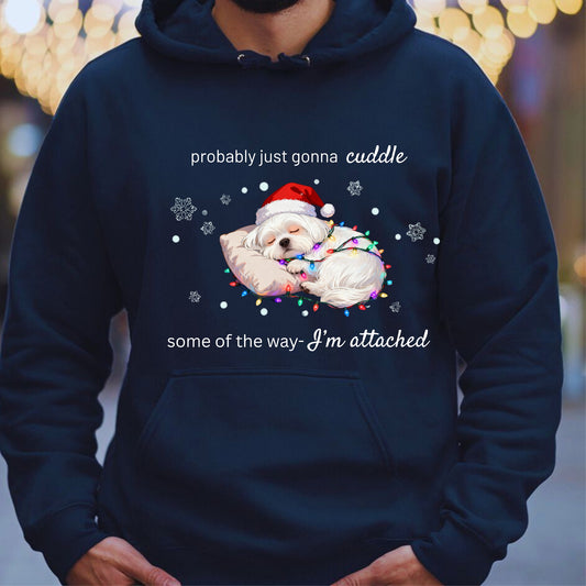 Navy blue hoodie with a Christmas-themed design featuring a dog in a Santa hat and lights, text 'probably just gonna cuddle some of the way I'm attached' on a blurred background.