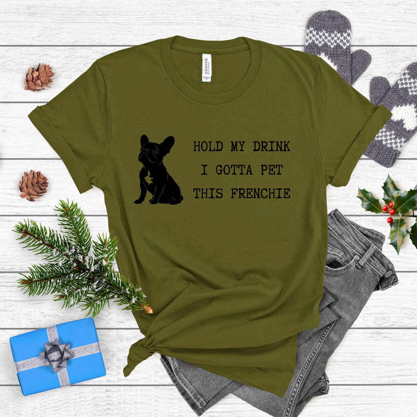 Green t-shirt with a dog graphic and text on a wooden surface with festive items.