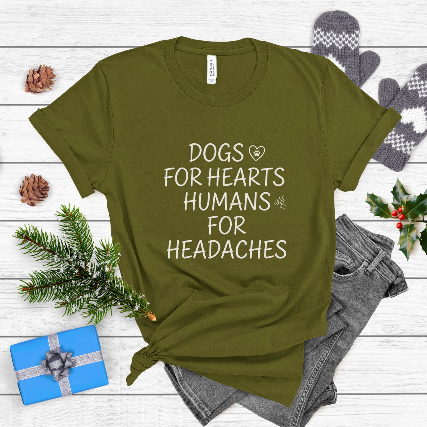Green t-shirt with text 'DOGS FOR HEARTS HUMANS FOR HEADACHES' on a wooden surface with festive items.