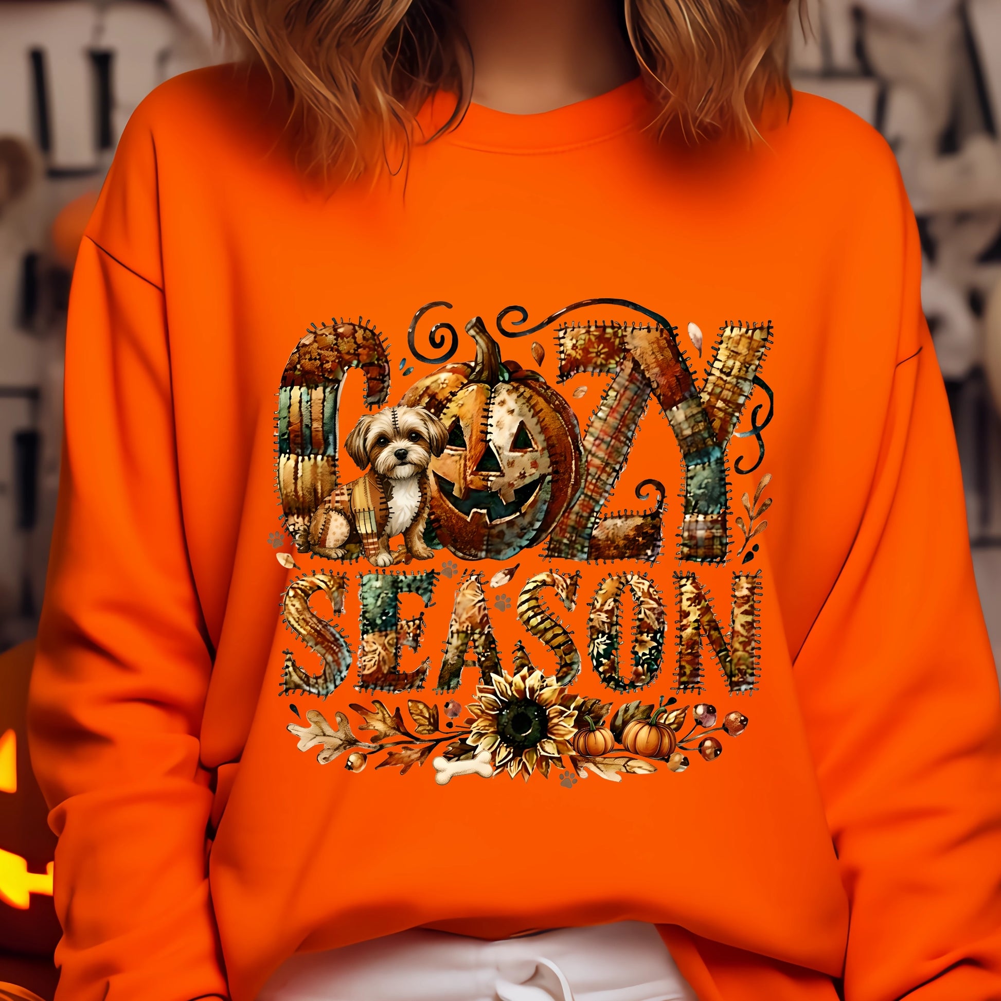 Person wearing an orange sweatshirt with 'Cozy Season' and Halloween-themed design.