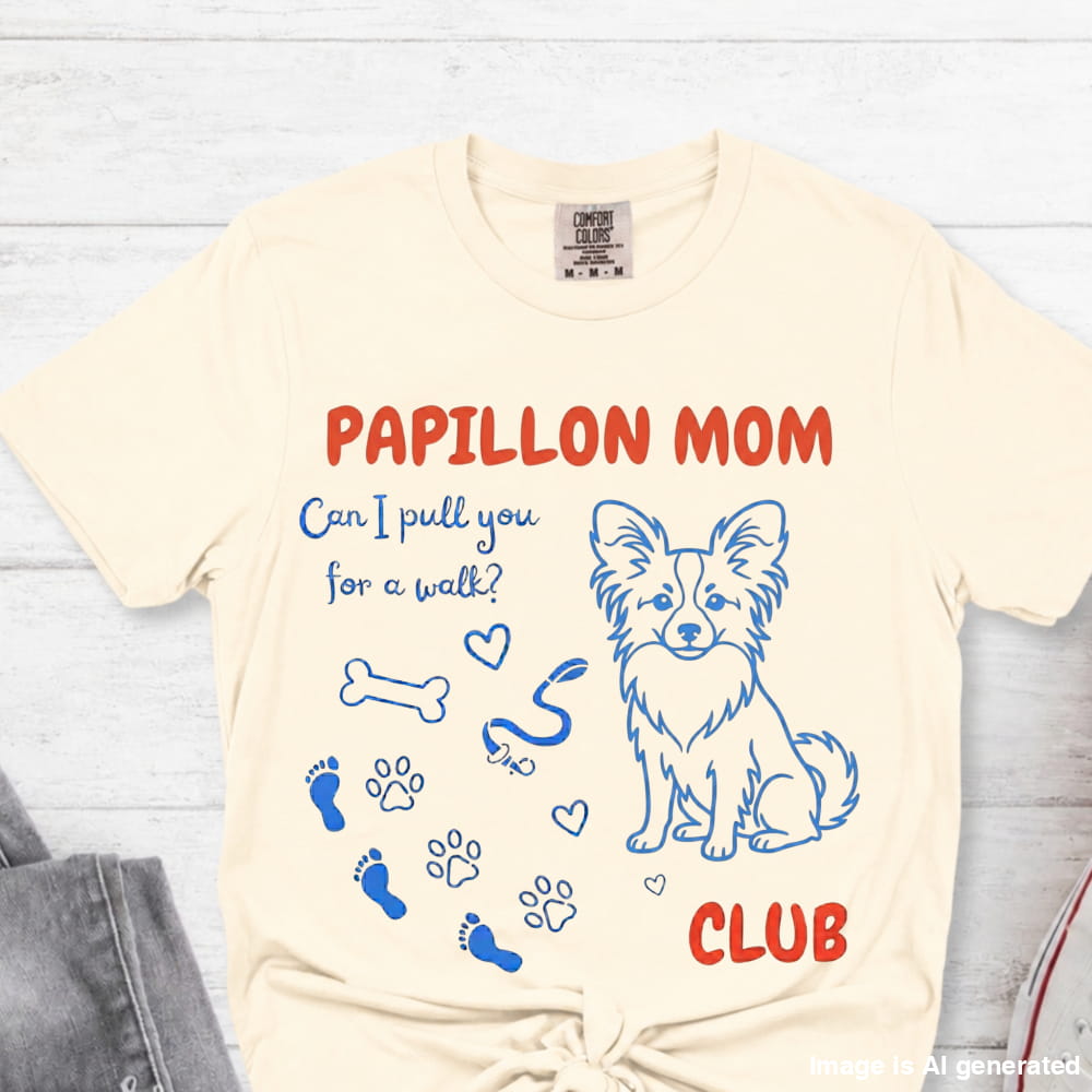 Beige t-shirt with Papillon dog graphic and text on a light wooden surface