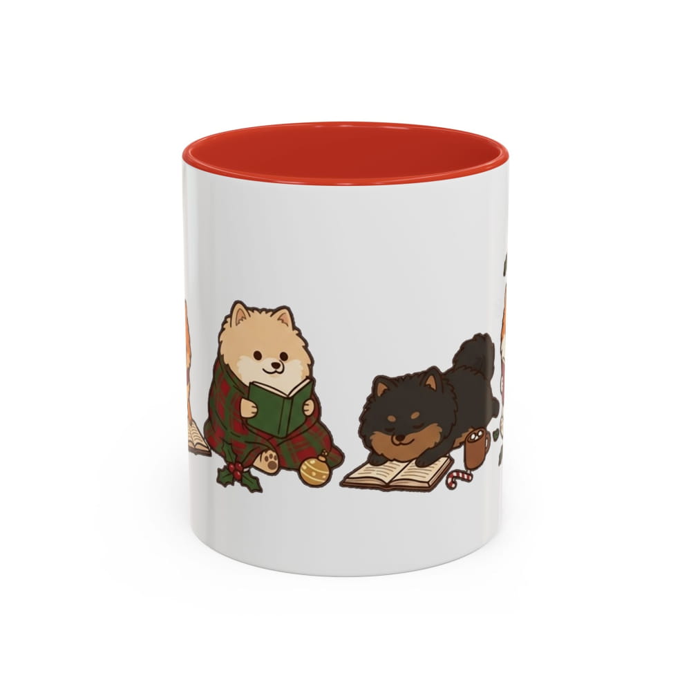 White ceramic mug with a red interior, showing a cream Pomeranian in a plaid blanket reading a green book beside a black Pomeranian lying on an open book.