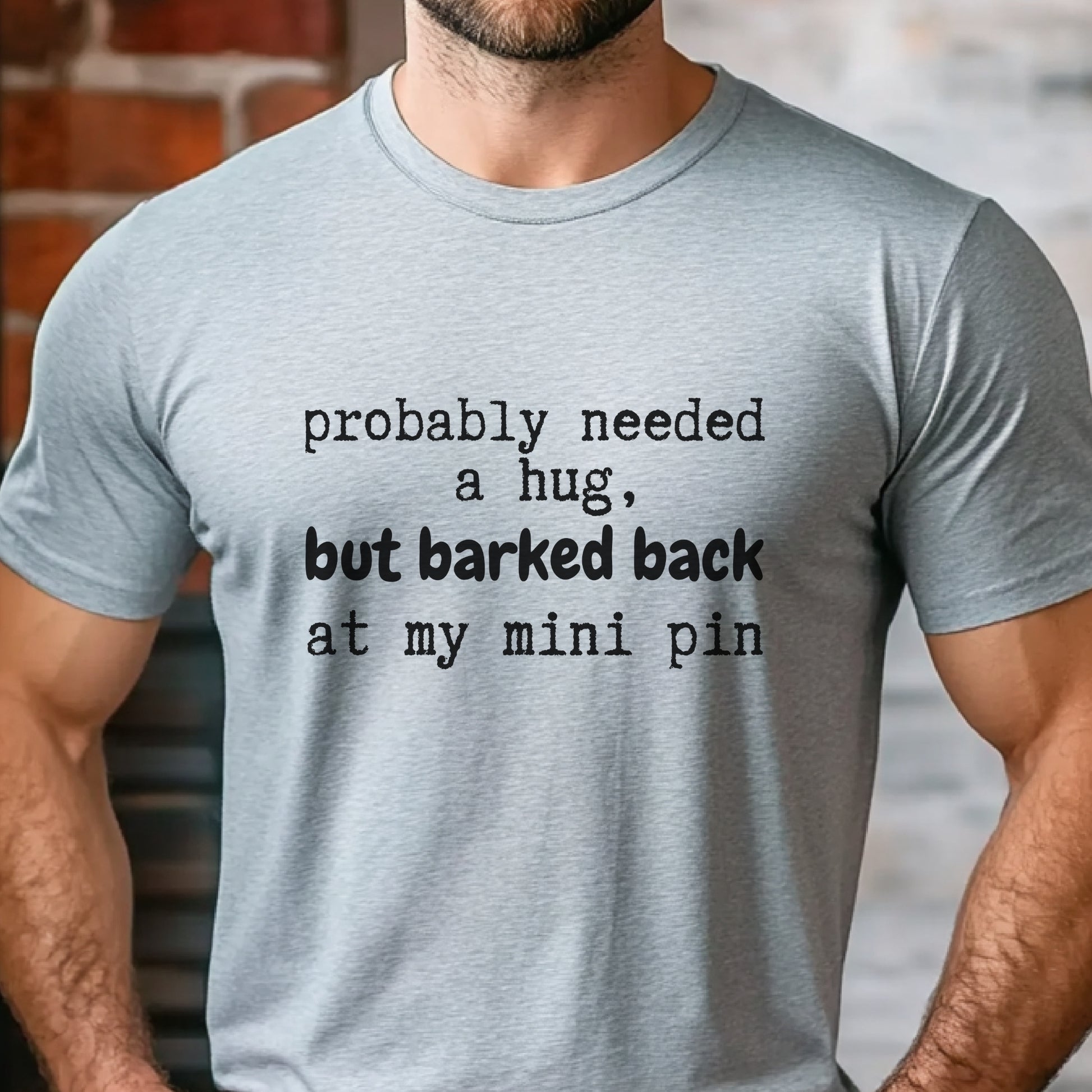 Grey unisex t-shirt with white text: "probably needed a hug, but barked back at my mini pin" centered on the chest