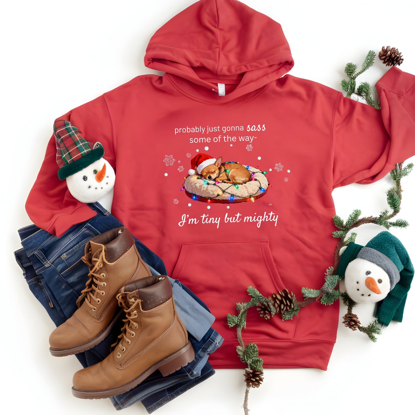 Red hoodie with Christmas-themed design, boots, jeans, and holiday decorations on a white background