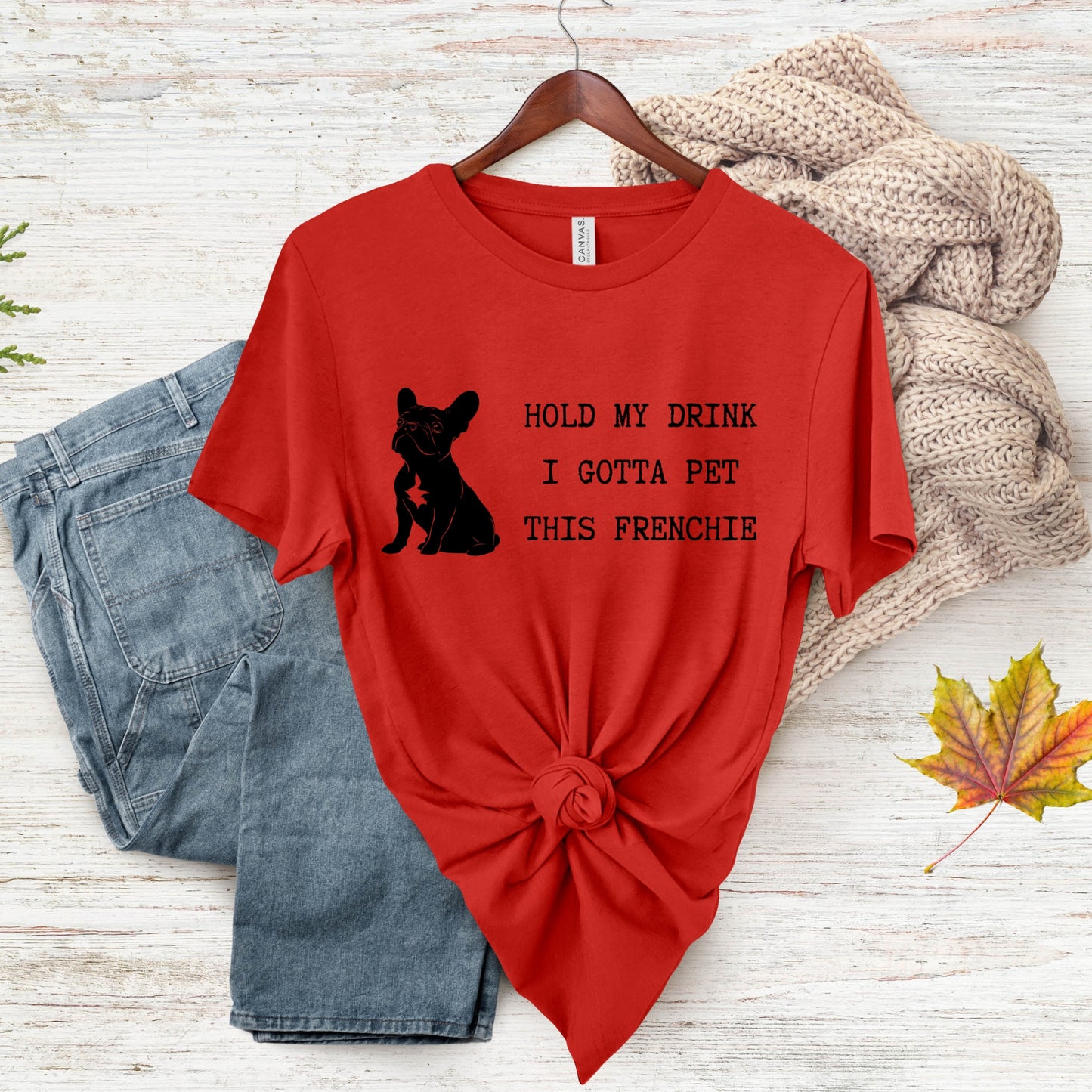 Red t-shirt with a dog graphic and text on a wooden surface with jeans and a sweater.
