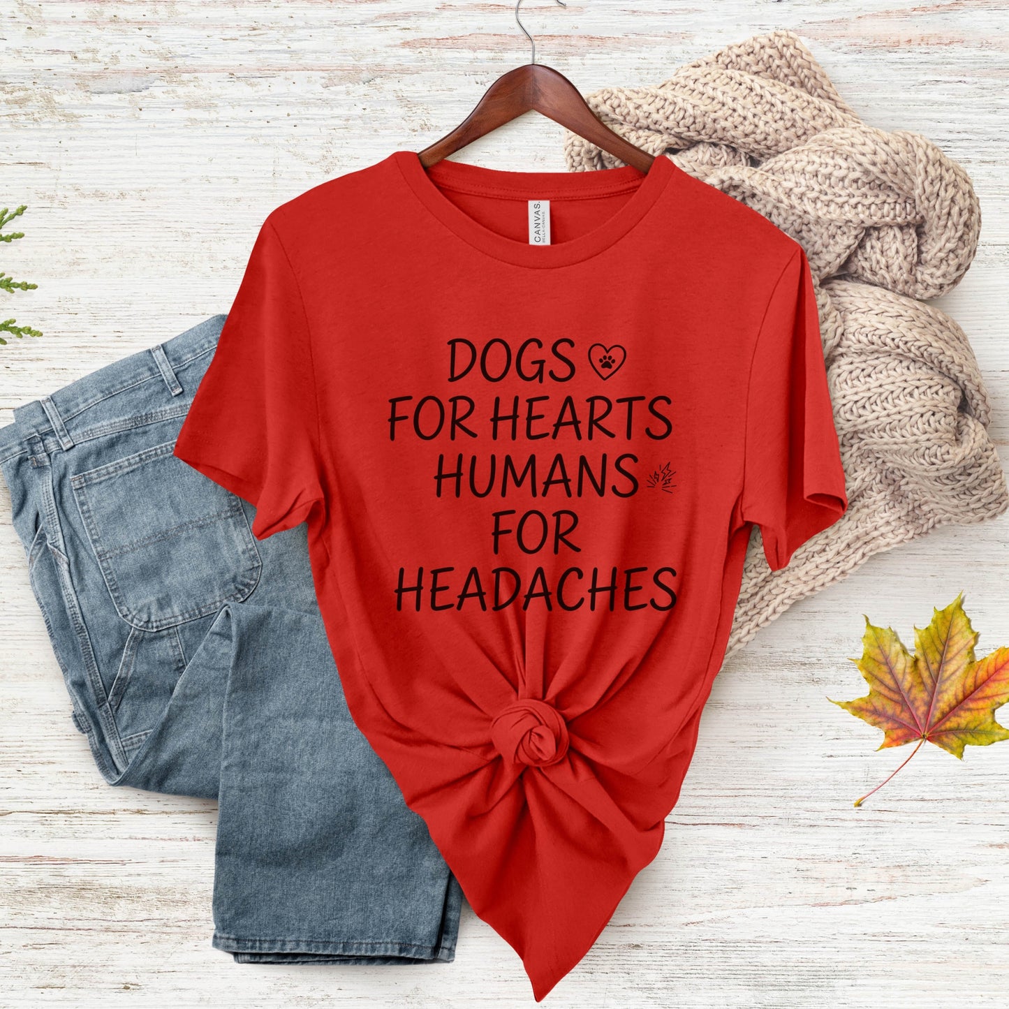 Red t-shirt with text 'DOGS FOR HEARTS HUMANS FOR HEADACHES' on a wooden surface with jeans and a sweater.