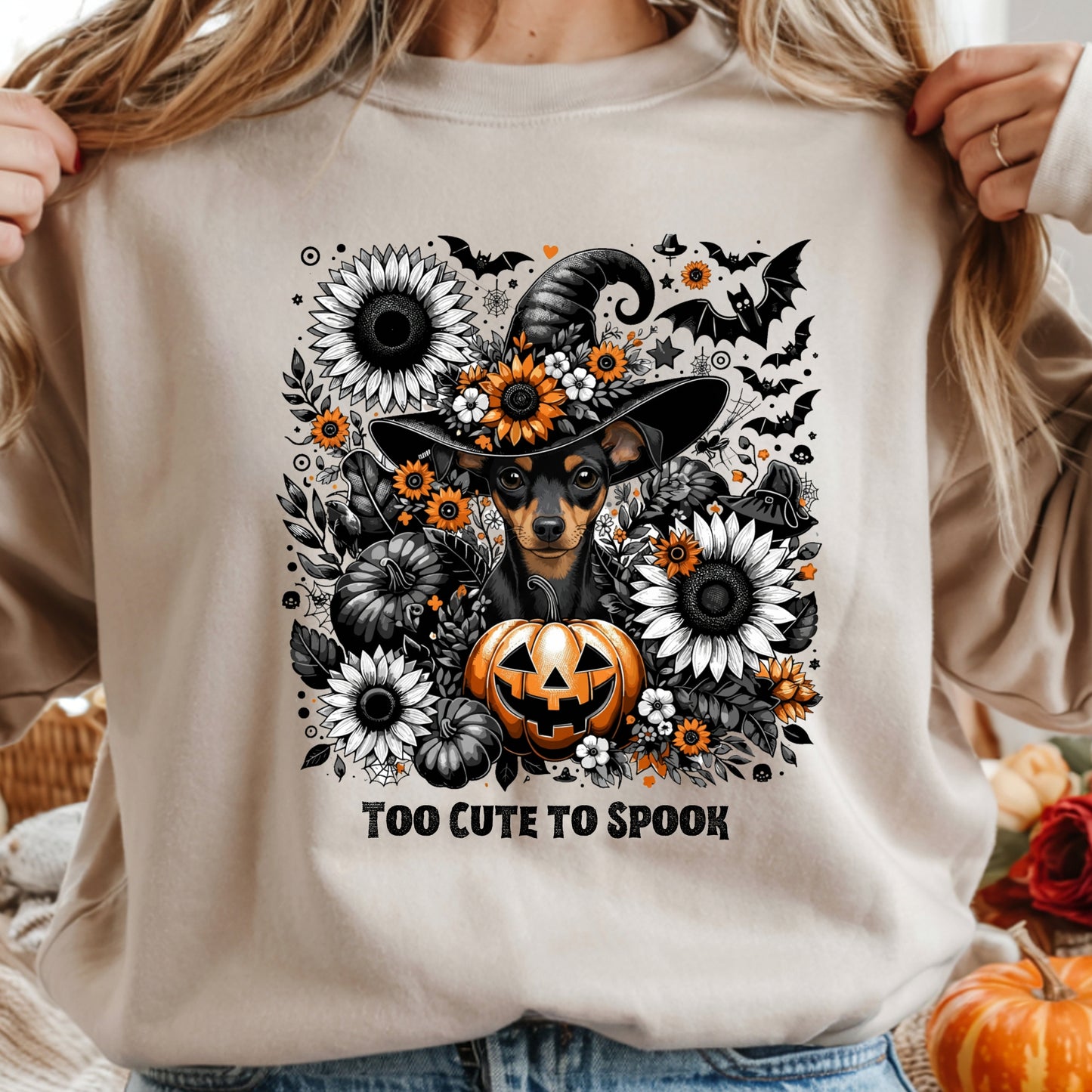 Beige sweatshirt with Halloween-themed design featuring a dog in a witch hat, pumpkins, and flowers.