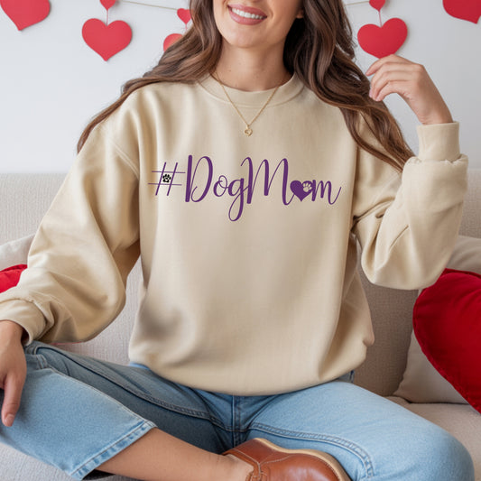 Person wearing a beige sweatshirt with '#DogMom' text, sitting on a couch with heart decorations in the background.